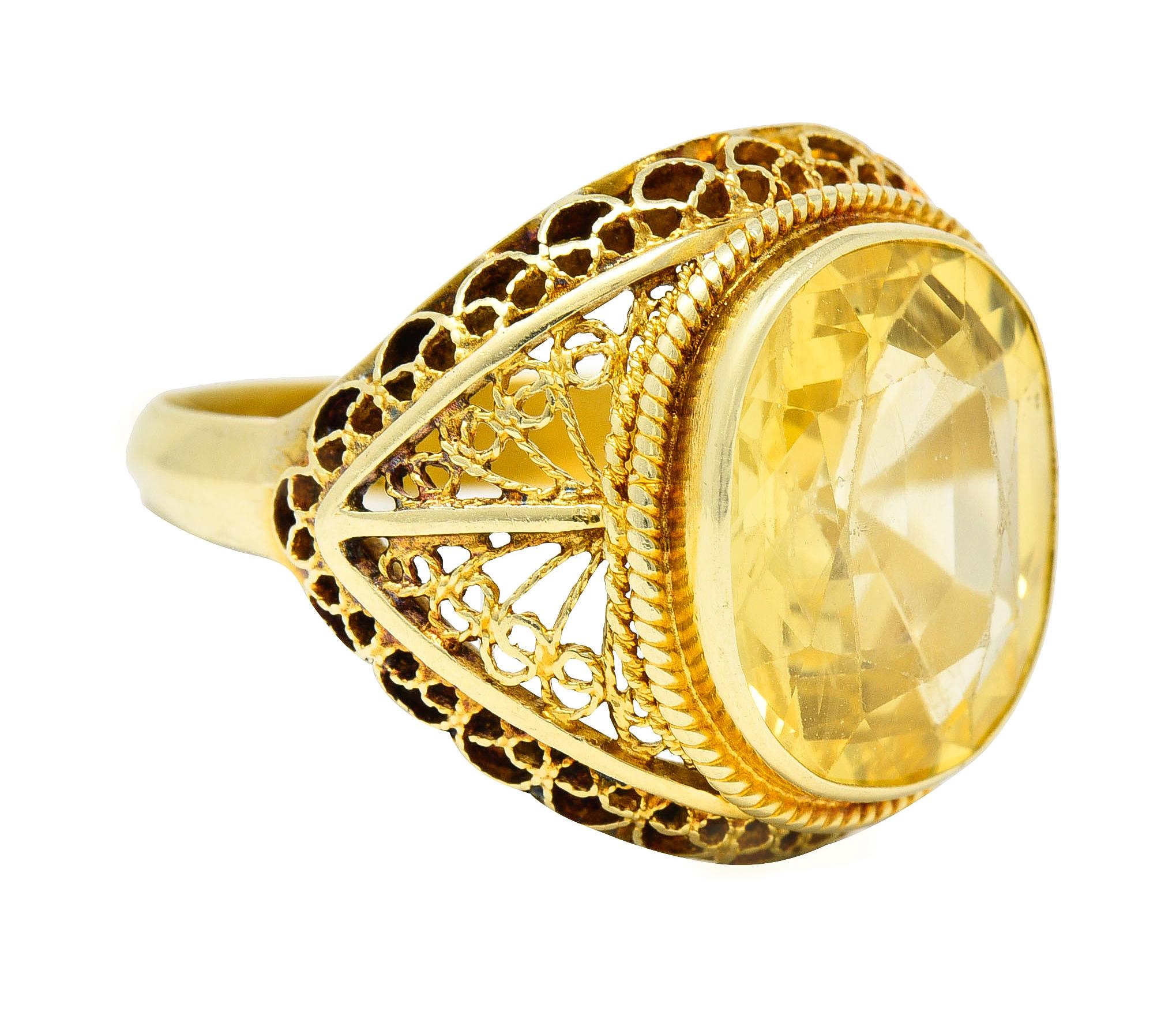 Centering a cushion cut sapphire weighing approximately 9.05 carats
Transparent medium yellow in color - bezel set
Accented by a twisted wire surround
Featuring a scrolling filigree bombay shaped gallery
With a pierced whiplash motif profile
Stamped