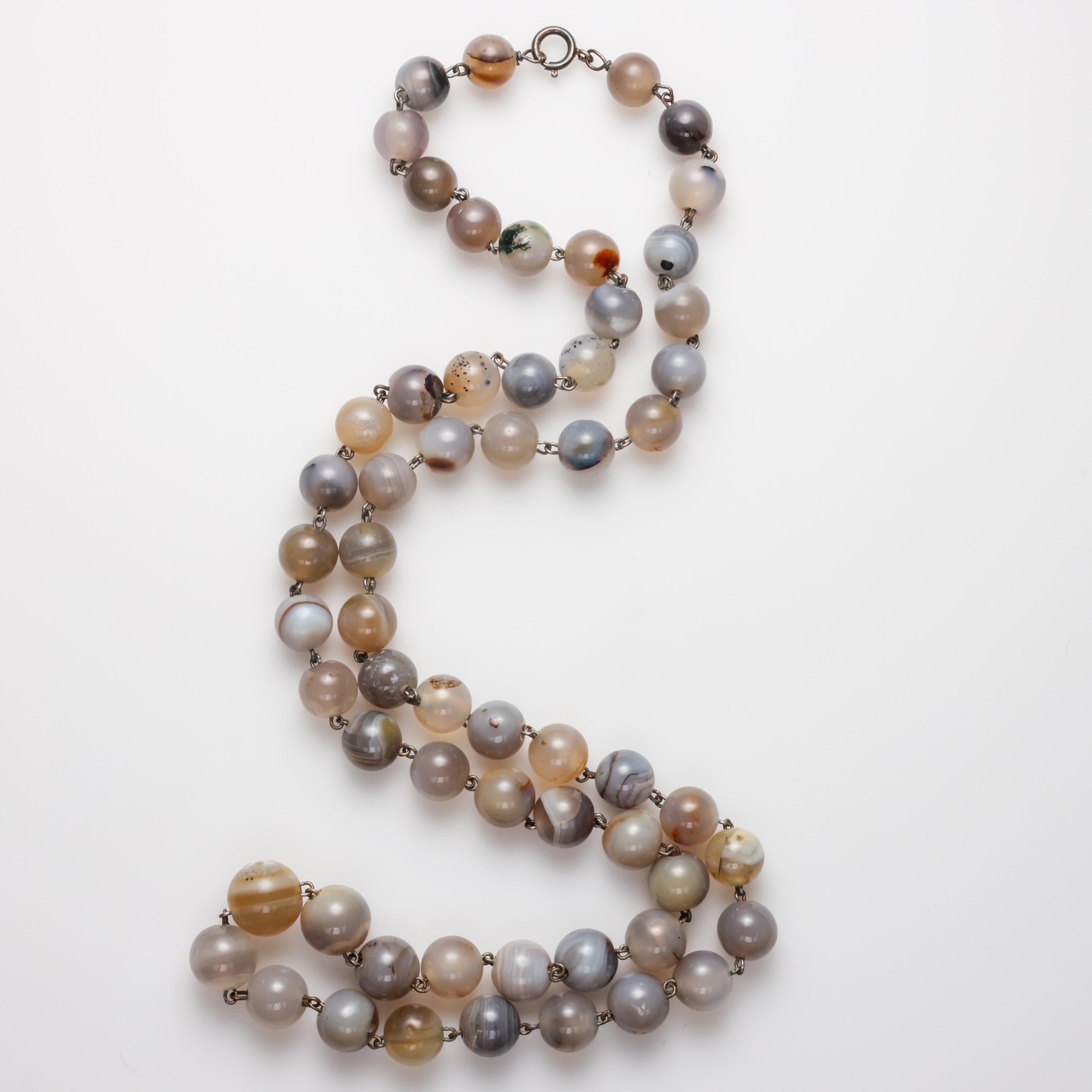 This is a gorgeous, original Arts & Crafts era (circa 1900) features 59 hand-carved round agate beads measuring 10mm to 14m, linked with hand-twisted silver wire. The spring clasp appears to be original to the piece. 

A luxurious 34