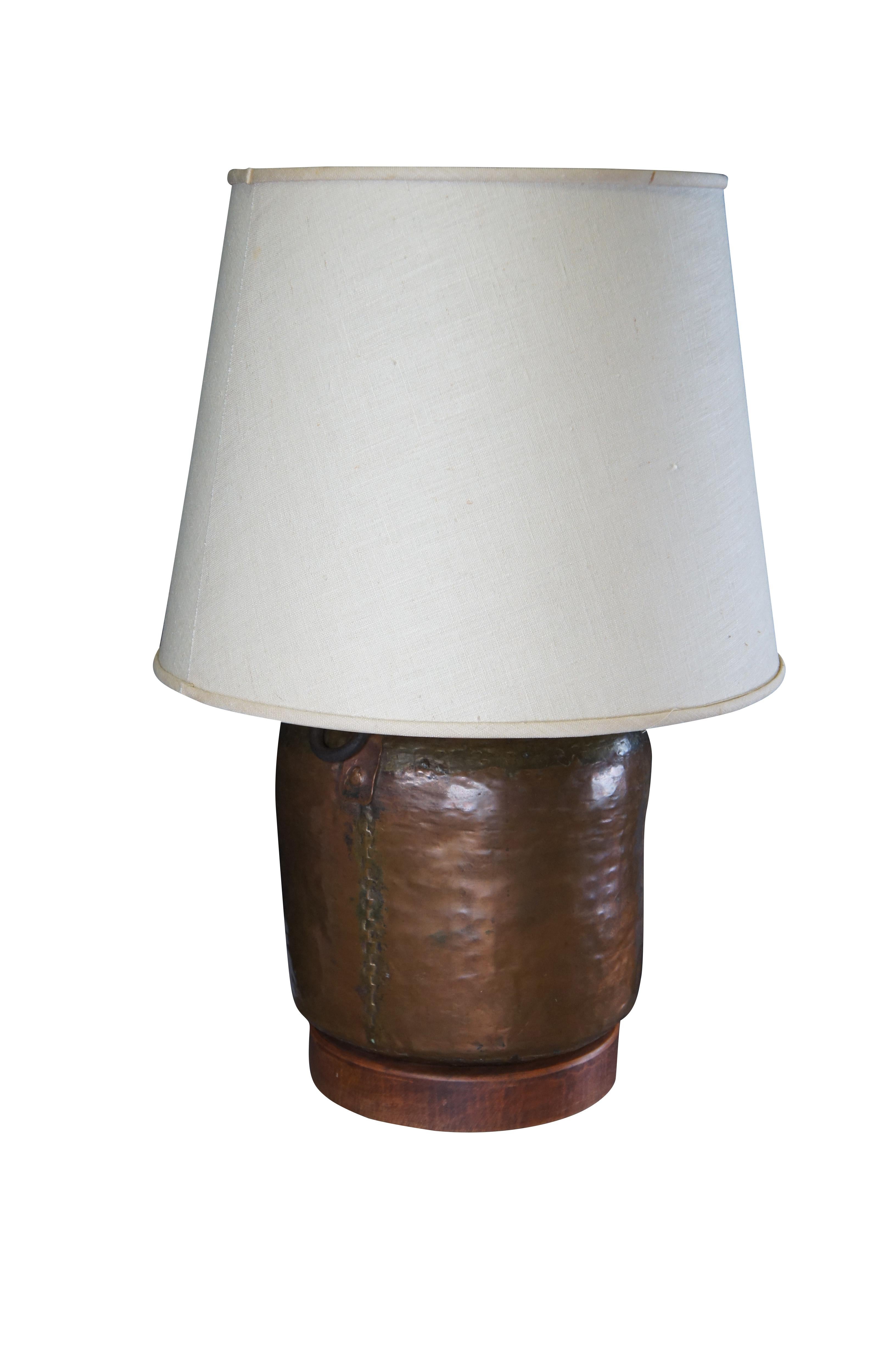 A beautiful antique hammered and dovetailed copper pot or canister table lamp.  The rustic 19th century pot has a unique form and charming patina.  Includes two iron handles and sits on a wooden plinth base.  The pot was converted to a lamp around