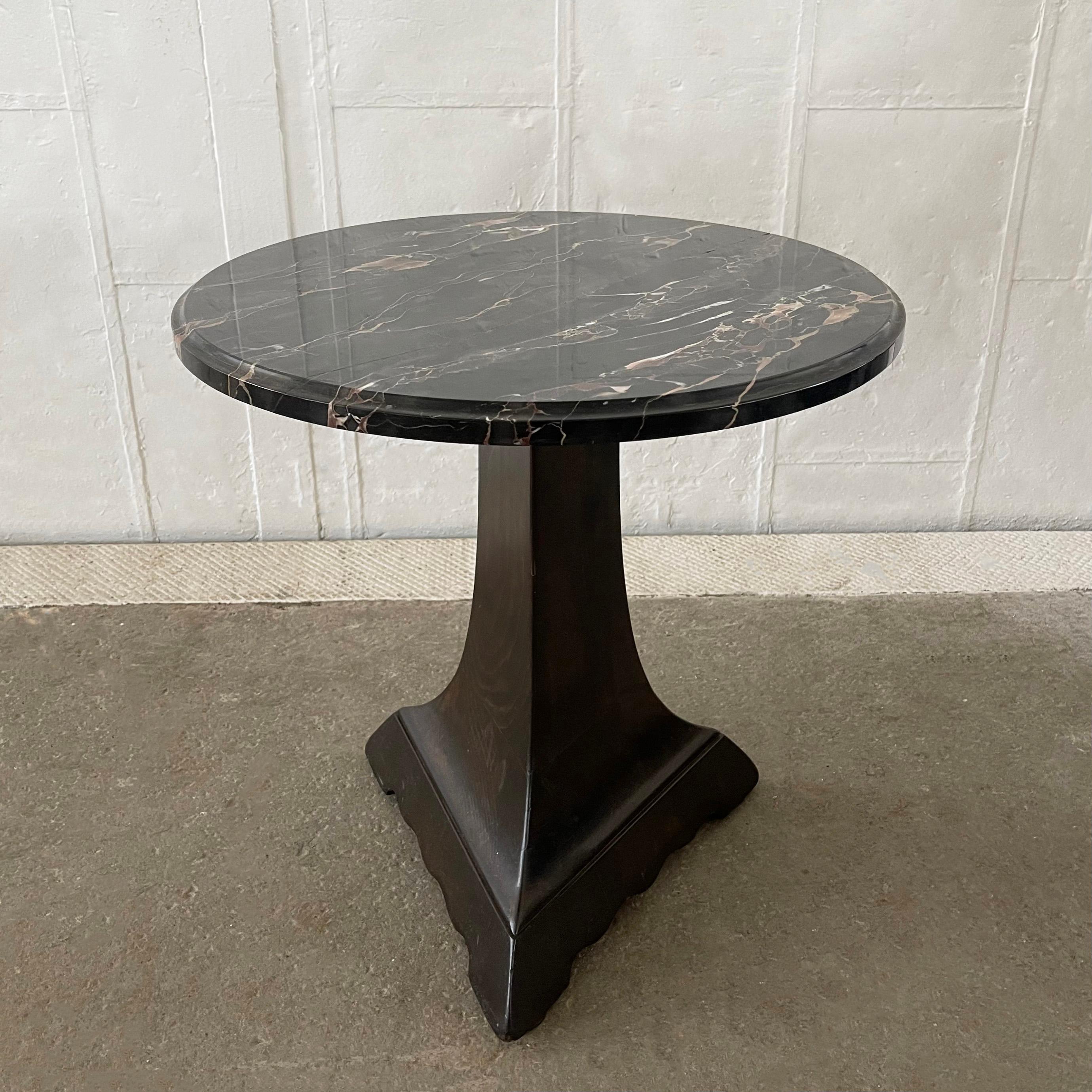 Charming, arts & crafts, occassional side table features a round black marble top with cove edge atop a lacquered triangular pedestal base with scalloped edge. 