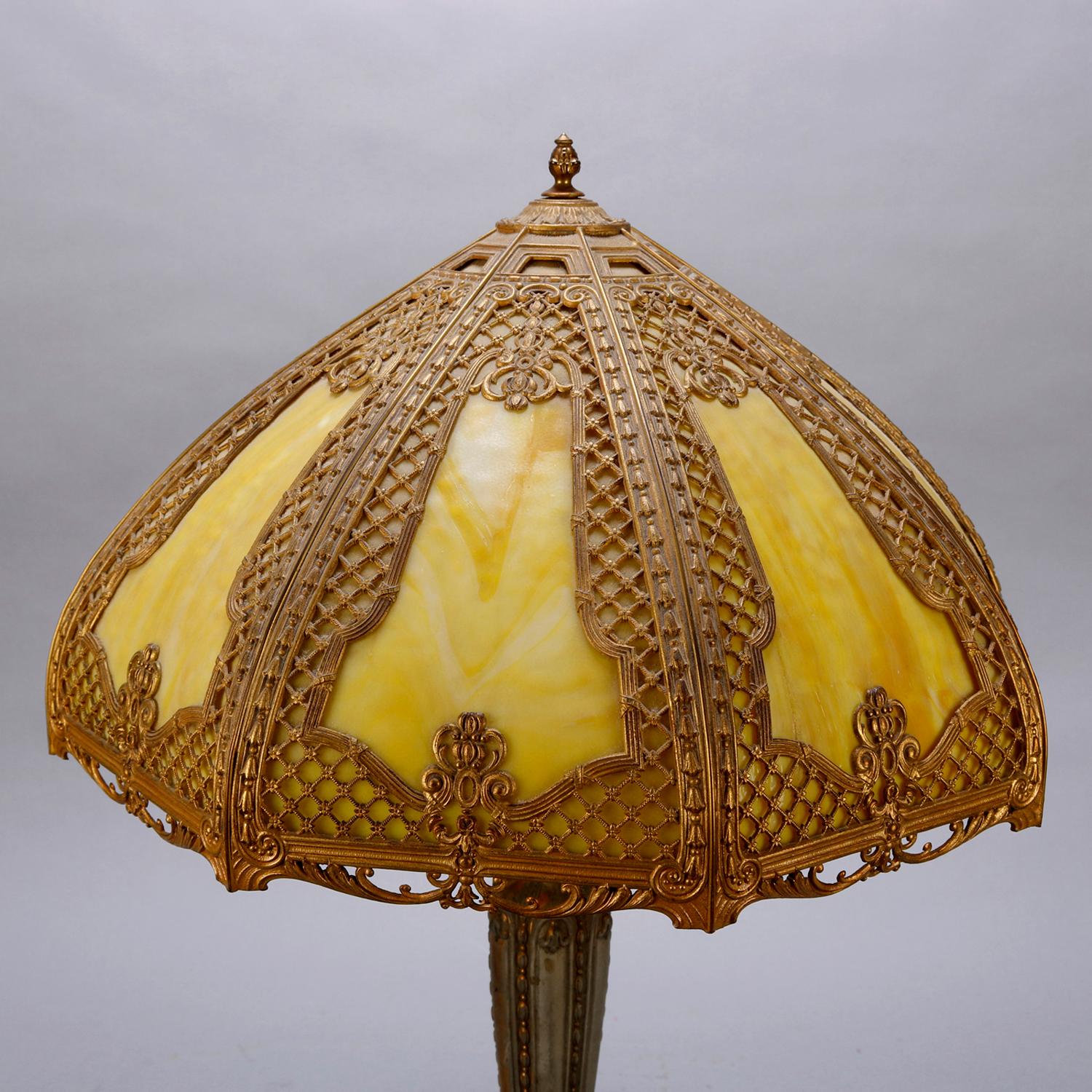 An Arts & Crafts table lamp in the manner of Bradley and Hubbard offers shade with lattice and foliate filigree shade housing bent slag glass panels and surmounting cast and gilt urn form base, circa 1920

Measures - 26