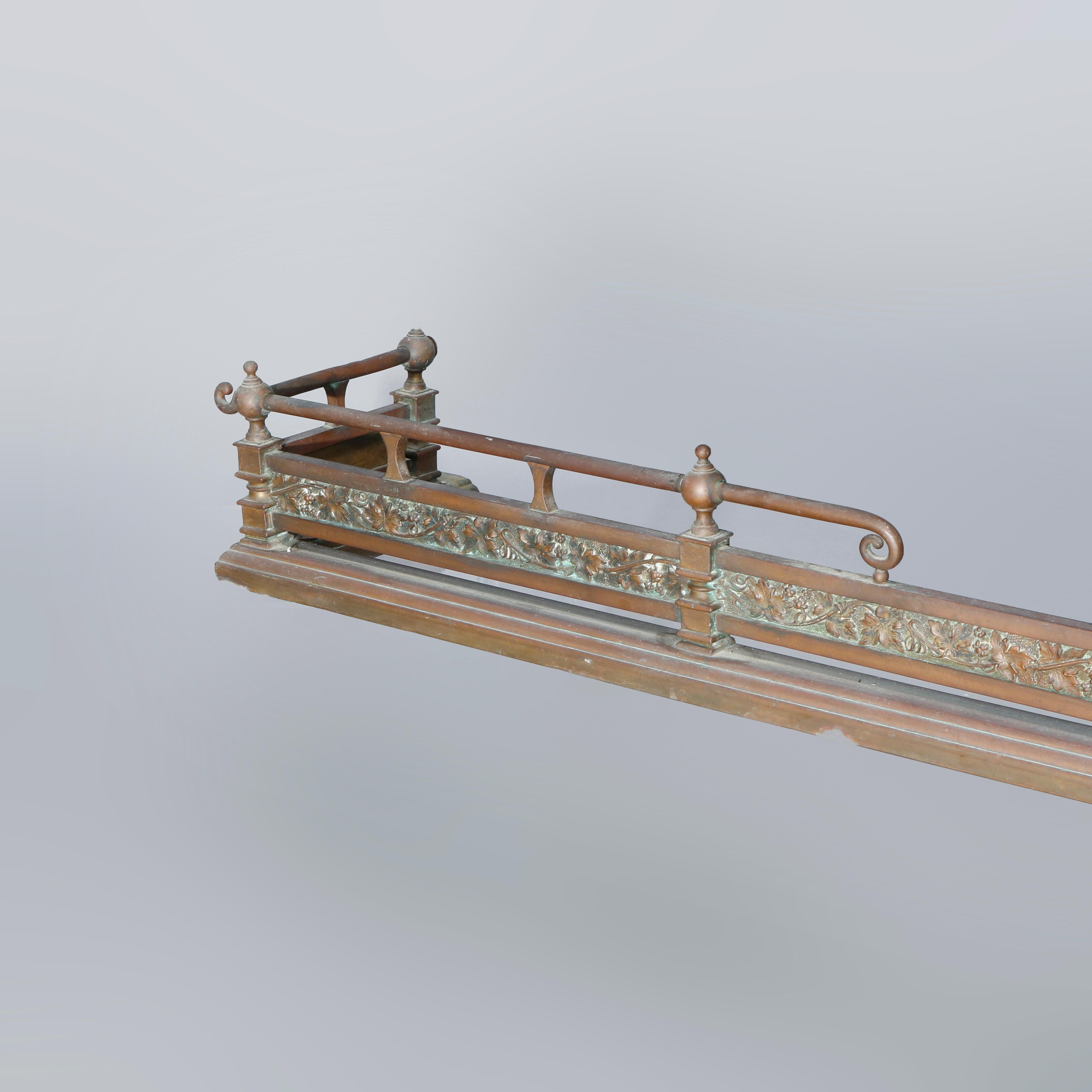 An antique oversized Arts and Crafts fireplace fender offers brass and bronze construction with split spindle rail with scroll elements over plate with vine and leaf in relief and having column form supports, c1900.

Measures: 7