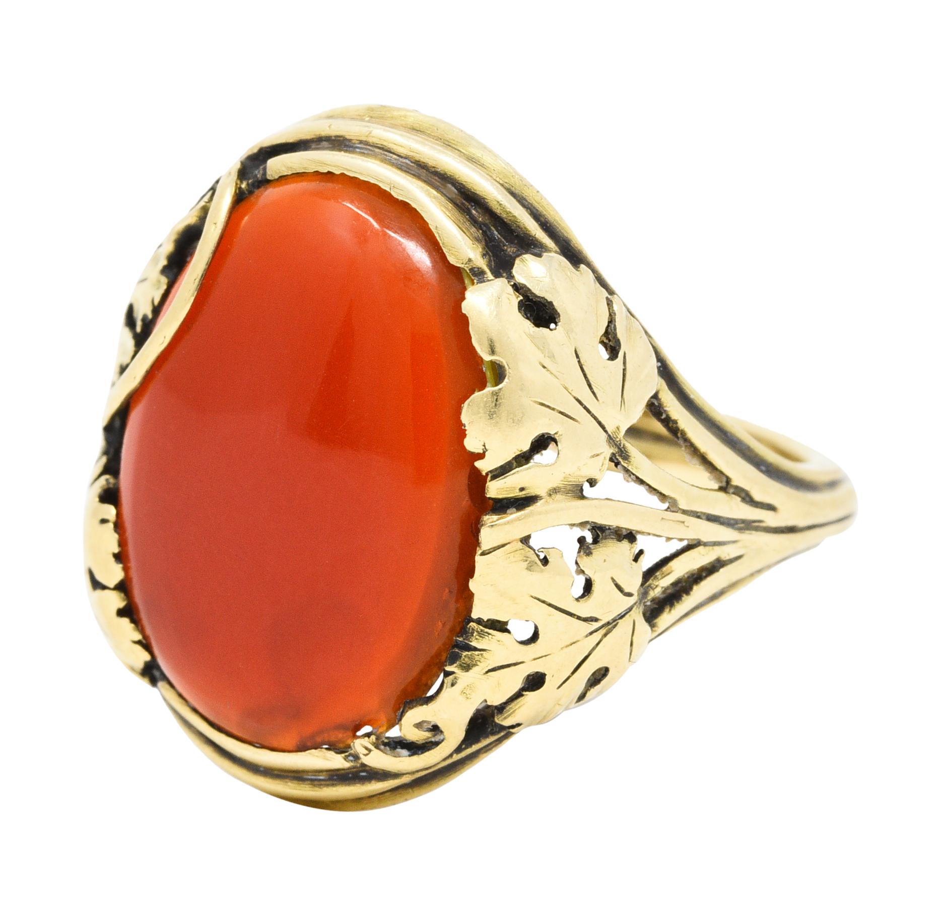 Centering an oval cabochon of carnelian measuring approximately 15.0 x 11.5 mm

Translucent with robust brick red color

Half bezel set with stylized and highly rendered leaf motifs

Completed by split shoulders and deeply ridged gold