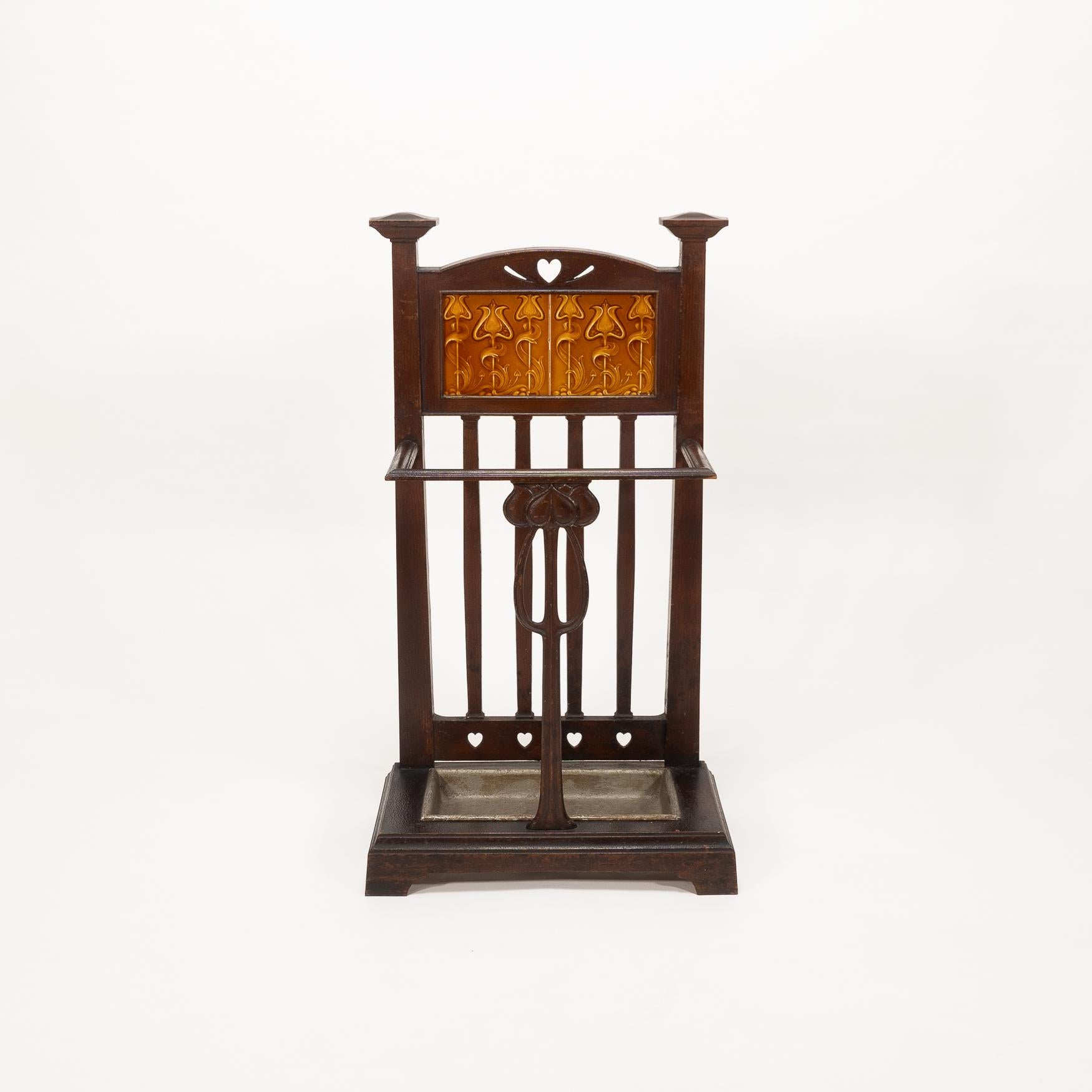 Canne et porte-parapluie en fonte de style Arts and Crafts
avec une finition peinte originale de style bronze. Les épis de faîtage sont coiffés d'un cœur percé au sommet et de carreaux de style floral Art nouveau au-dessous.
Sur le devant, une fleur