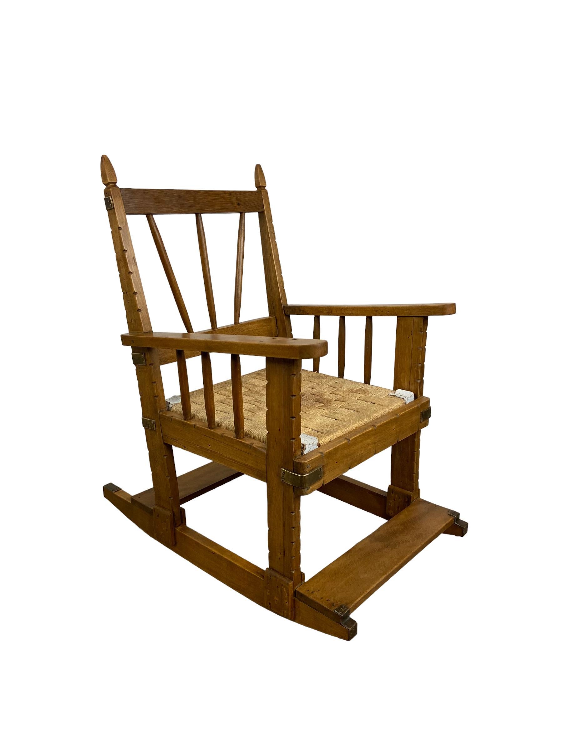 Stuhl im Arts-Crafts-Stil für ein Kind. Hergestellt aus Eichenholz in Frankreich in den 1920er Jahren. Der Sitz ist aus Papierschnur. Eine seltene Art von Schaukelstuhl, der leicht schaukelt und mit Kupferplatten verziert ist. Dieses Vintage-Objekt