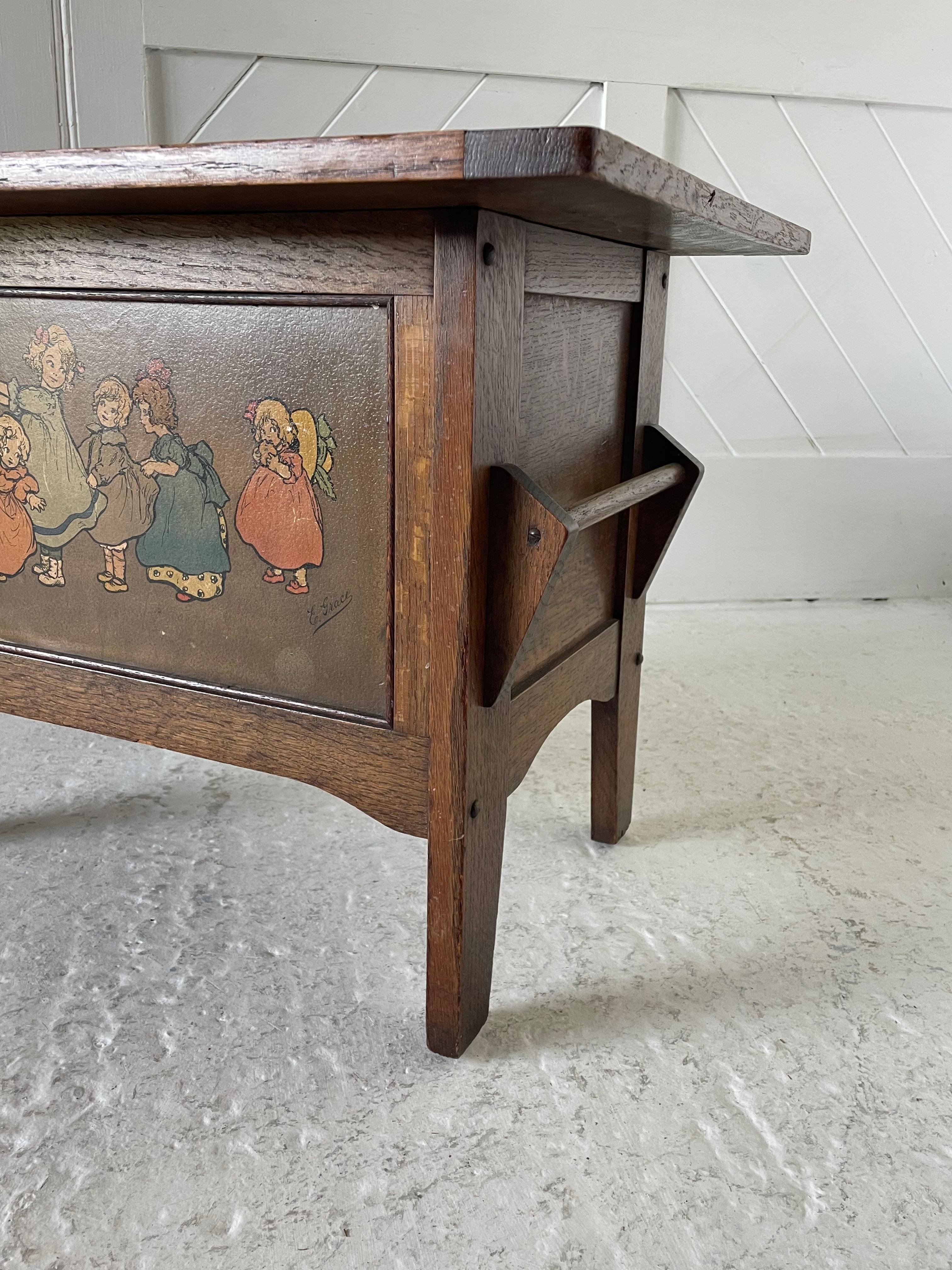 Coffre à jouets pour enfants en chêne de style Arts & Crafts avec porte-serviettes de chaque côté

Couvercle à ouverture à charnière

Panneau maternel en carton imprimé de couleur représentant des enfants en train de jouer

Signé E. Grace

Attribué