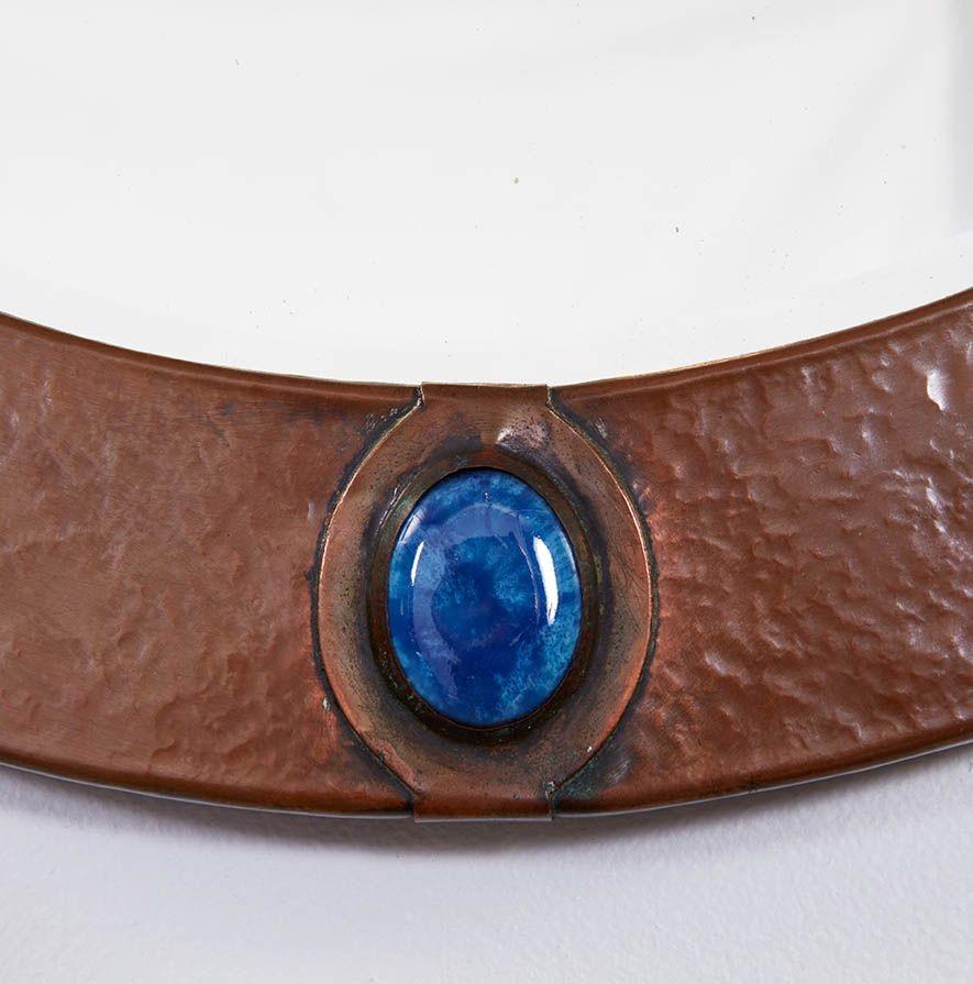 A round mirror in the style of Libertys, in hammered copper and featuring four blue cabuchons set in copper mounts at the compass points. Original beveled circular plate mirror glass. Good size and possessing a tailored, decorative look. English,