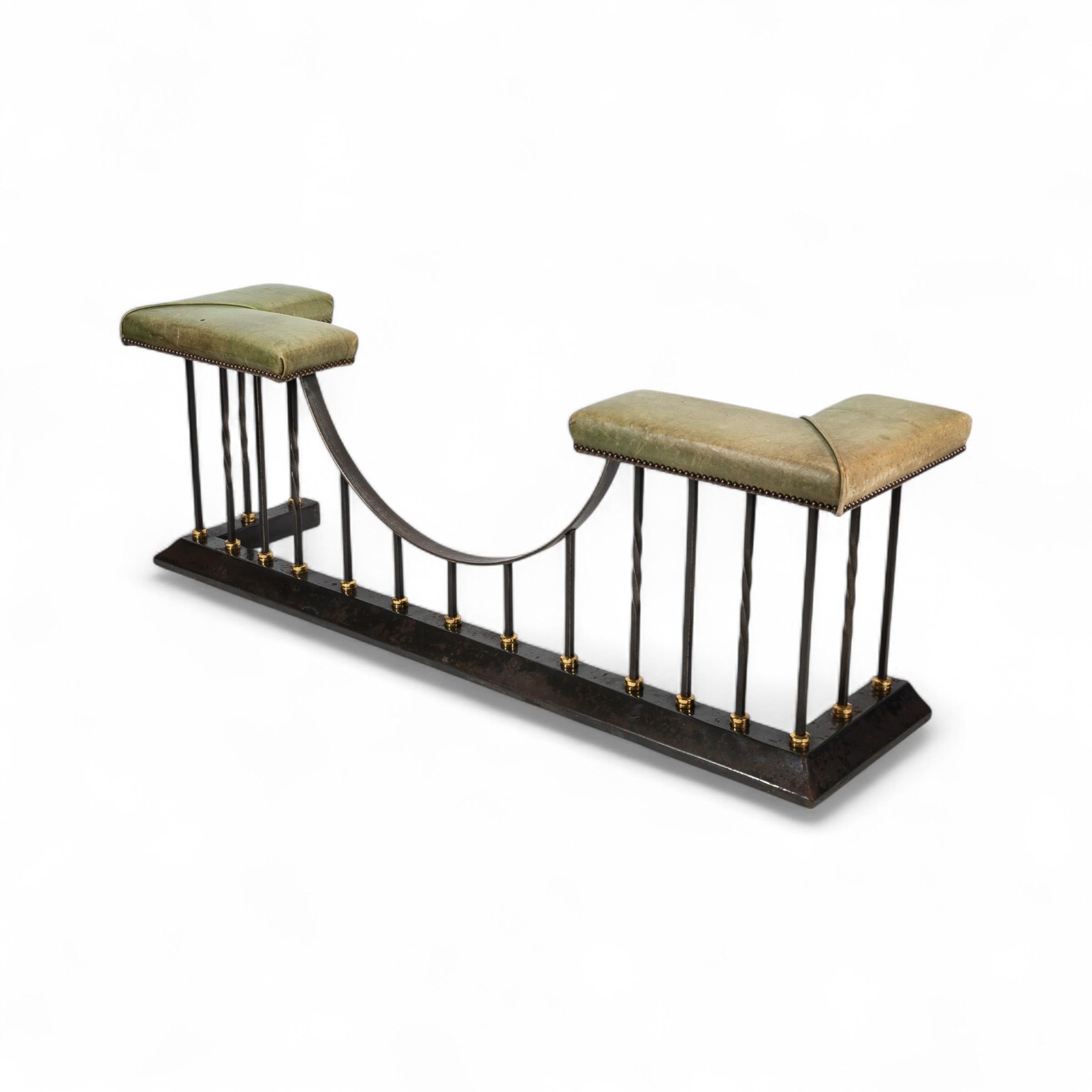 An Arts and Crafts club fender made of brass and cast iron, featuring green leather seats with stylised embossed motifs to the brass apron and uprights. The central panel is decorated with a flowing symmetrical design flanked by softly rounded