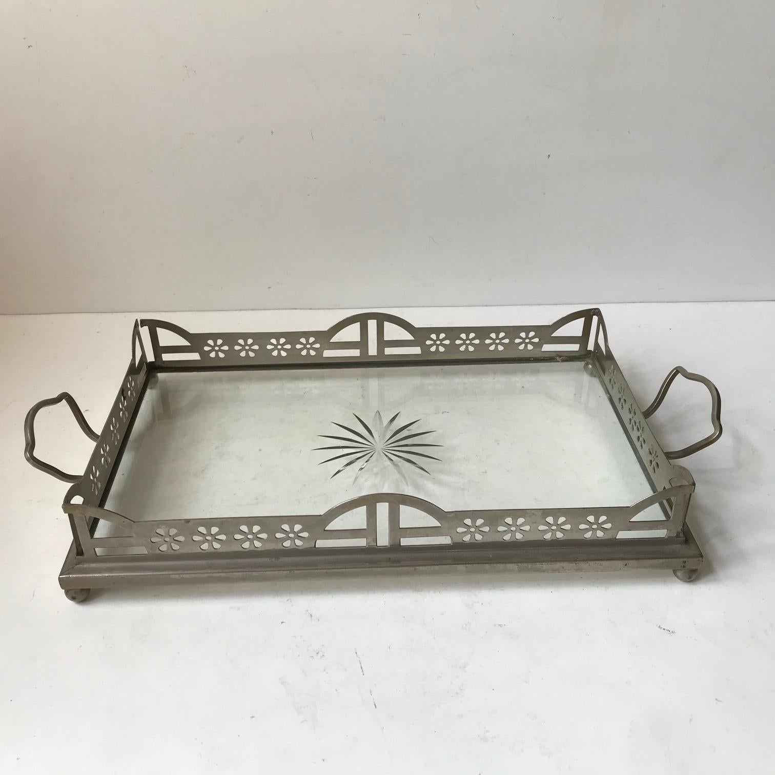 A wellkept small English Art & Crafts drinks or tea serving tray. It has a silver or nickel plated frame and a thick heavy quality glass top with a polished star decoration. It was made between 1875 and 1900. Measurements: 40 x 20 x 6 cm. It has no