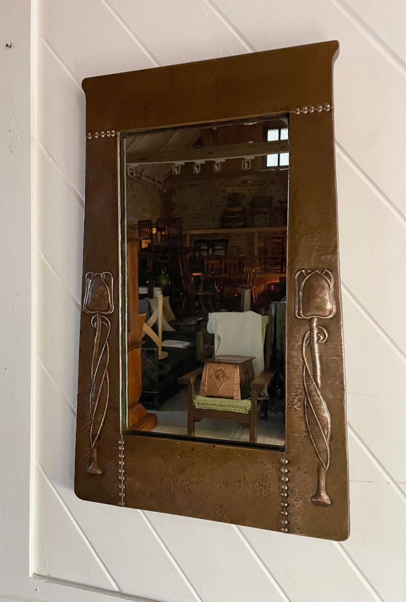 Arts & Crafts patinated copper framed mirror

With stylised decorative tulip design

Trapezium shaped frame hammered repousse work and rivet construction

Label to reverse

Liberty & Co

Circa 1900

Height 64cm. Width 39cm. Depth 2.5cm