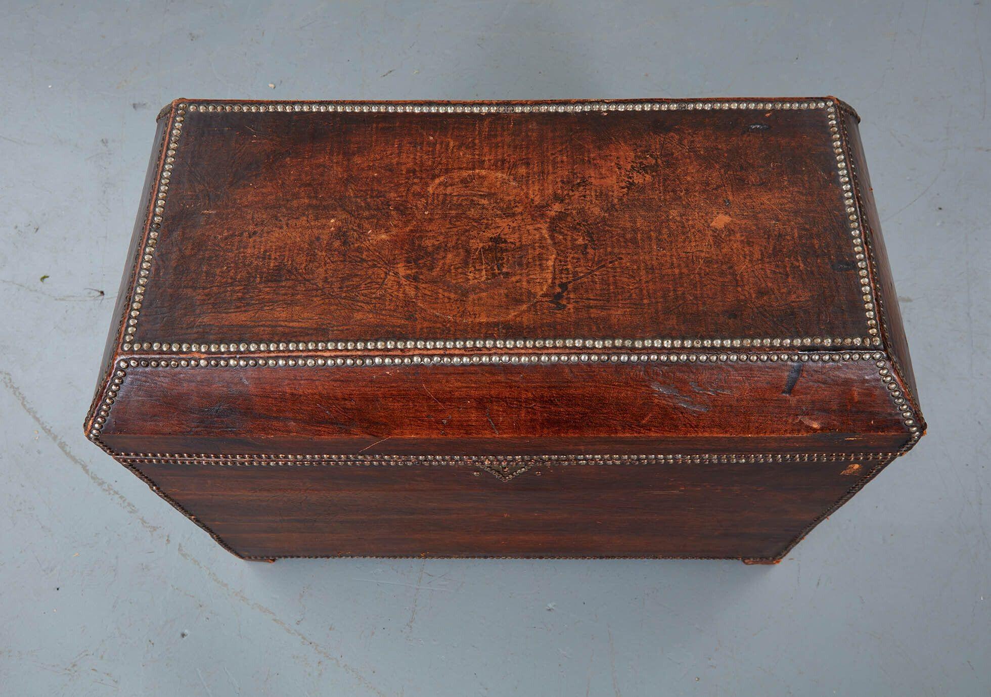 An Arts & Crafts leather covered and copper studded trunk with good patina to leather, beveled top and hand-forged wrought iron handles with star escutcheons and chased iron rings. Desirable flat top for use as a coffee table.