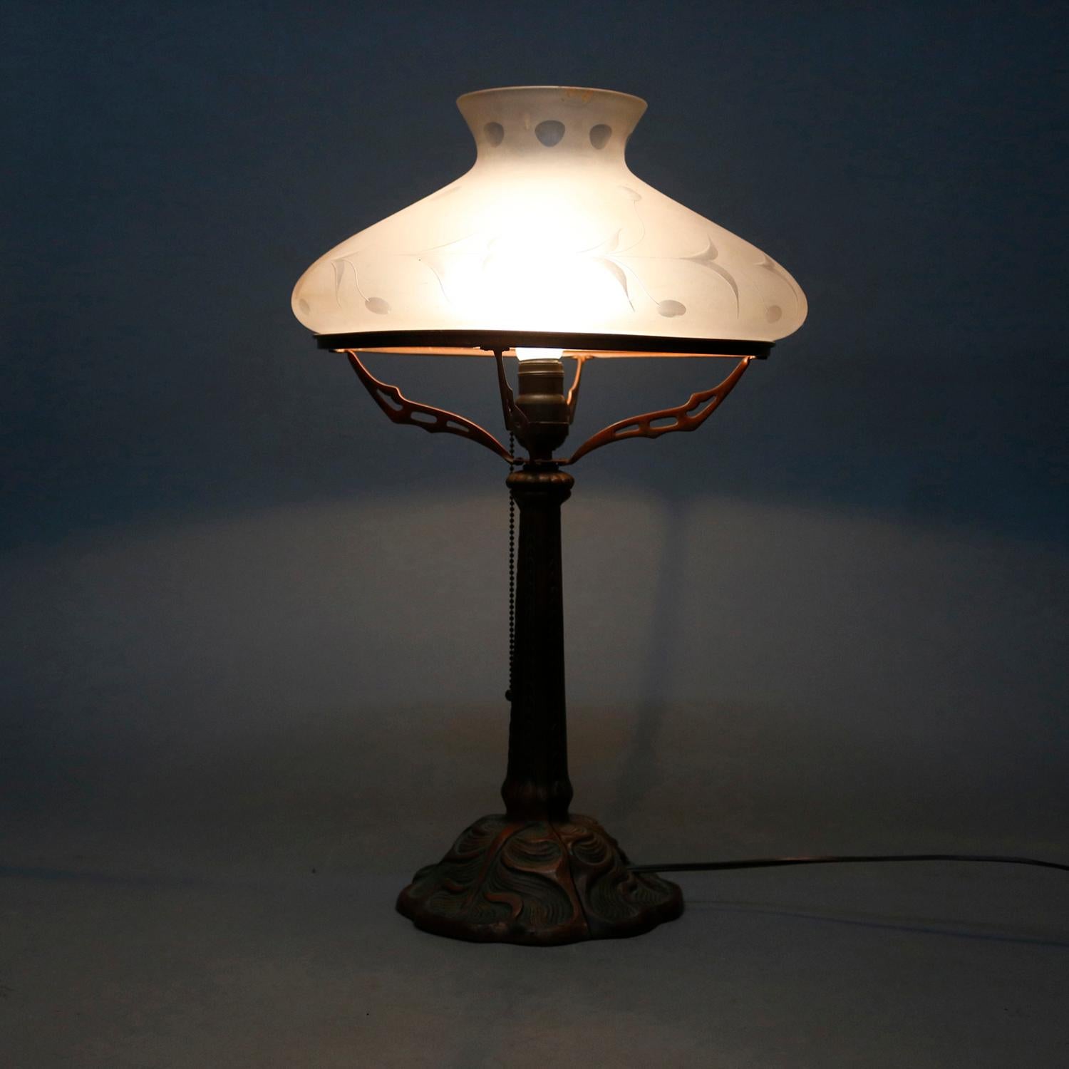 An Arts & Crafts single socket table lamp offers cast coppered metal base with Art Nouveau naturalistic elements surmounted by an acid etched tam-o-shanter shade, professionally re-wired, circa 1920

Measures: 23