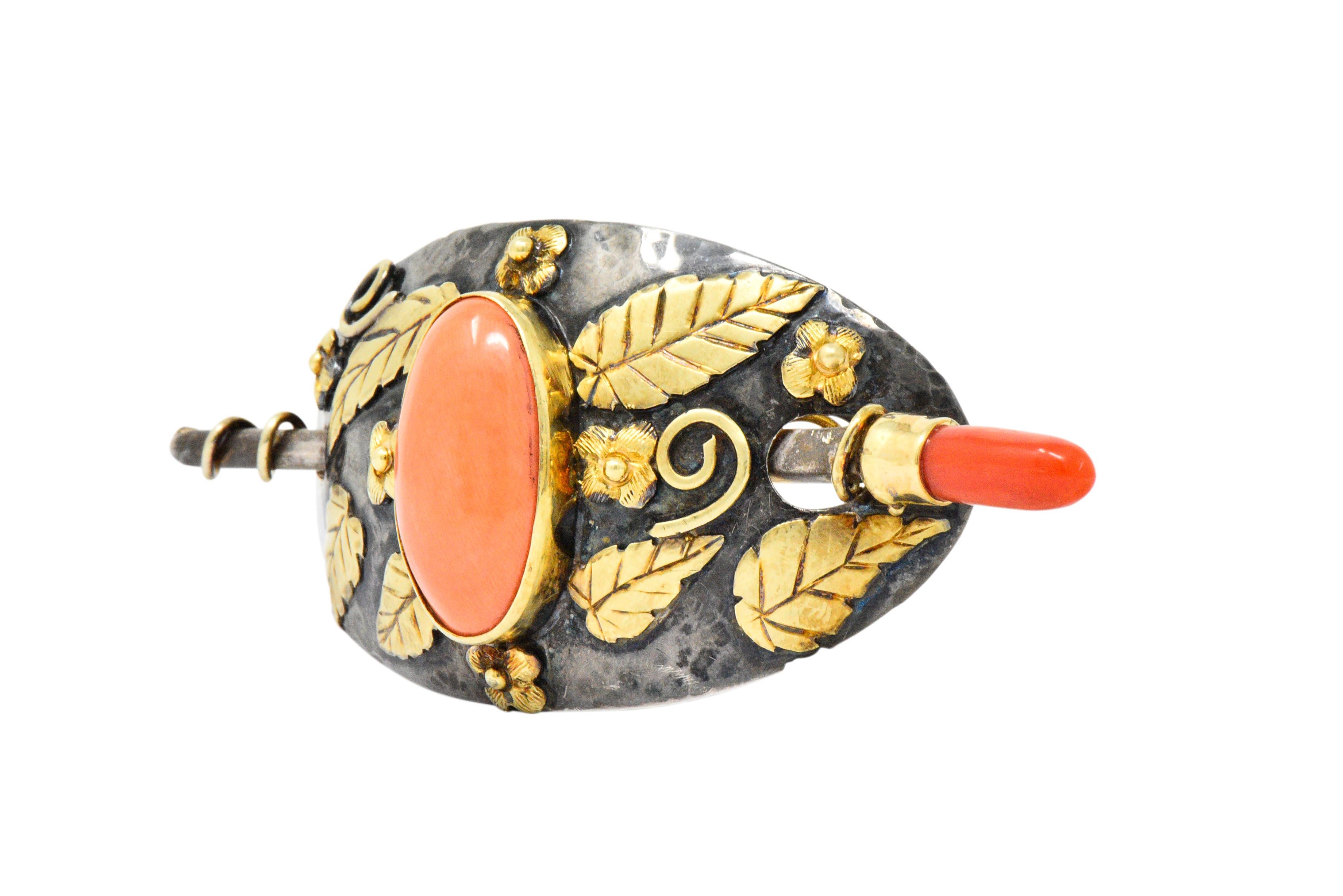 Originally a hair pin that has been converted to a brooch

Designed as a large oval comprised of hammered silver with floral and foliate gold appliqué

Centering an oval coral cabochon measuring approximately 23.7 x 13.0 mm

Bezel set in gold with