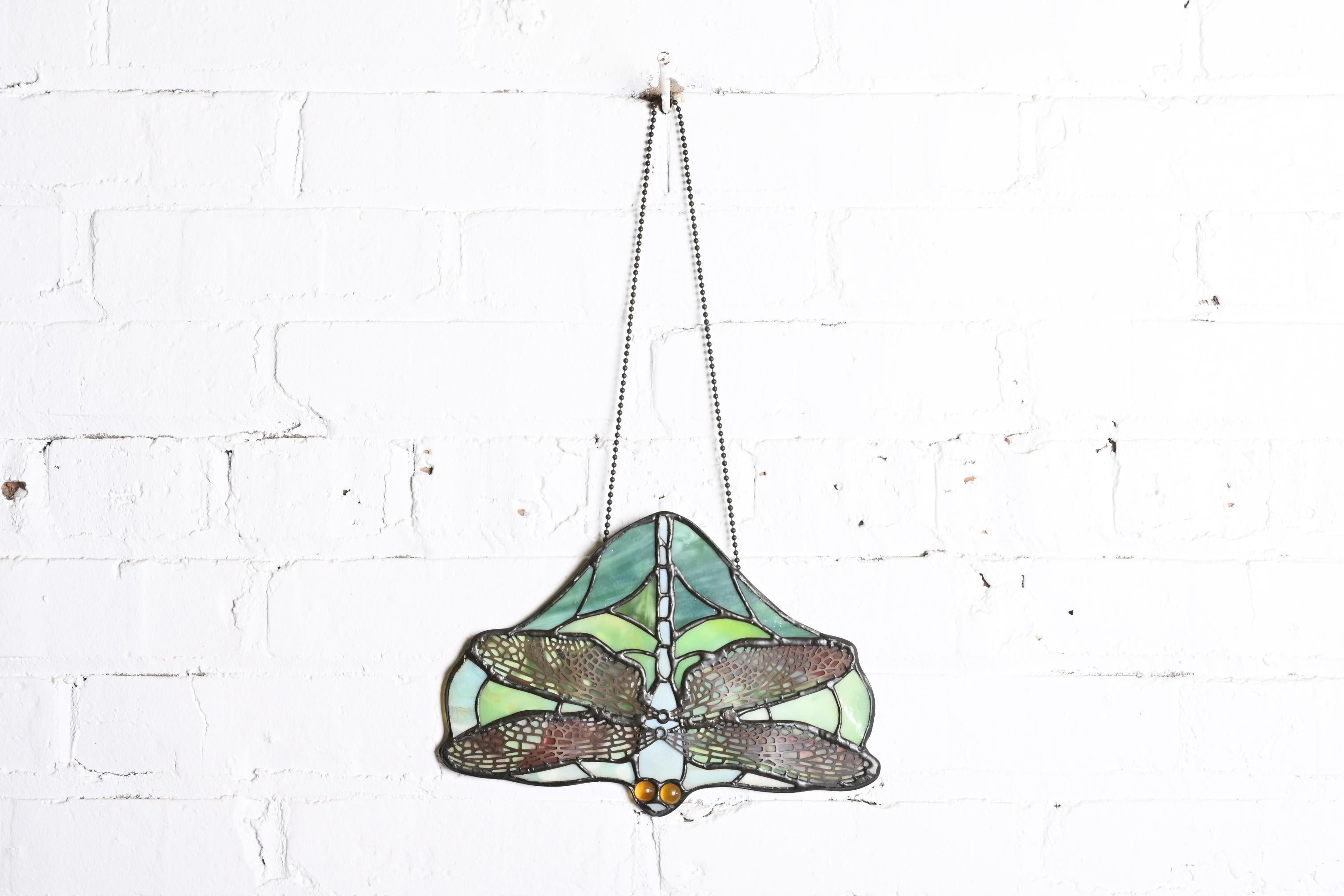 A gorgeous Arts & Crafts style stained glass window hanging, sun catcher, or lamp screen in the form of a dragonfly

In the manner of Tiffany Studios New York

USA, 20th Century

Stained glass, with copper wings and topaz jeweled glass