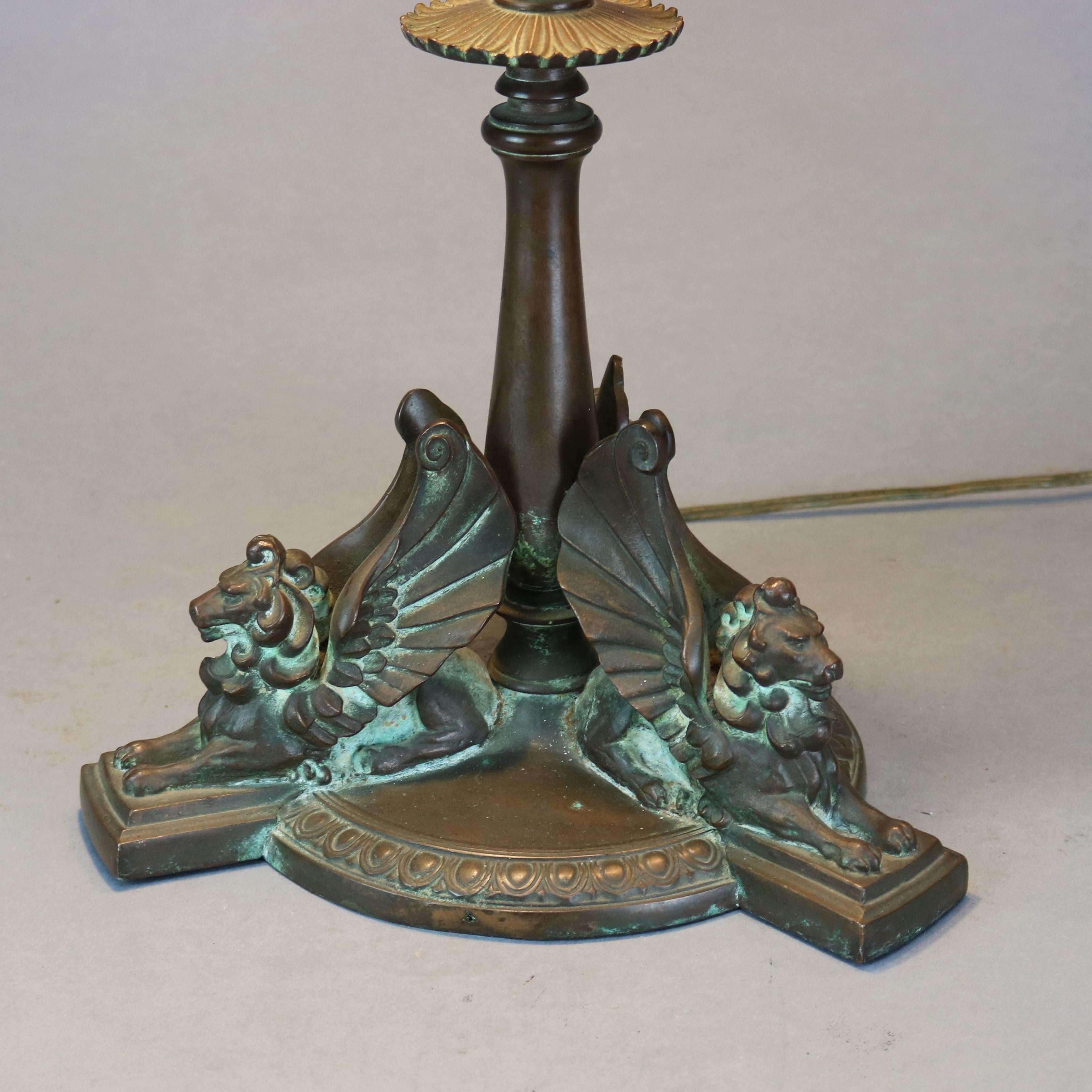 An antique and large Arts and Crafts table lamp by Handel offers mosaic leaded stained glass dome shade with water lily pattern surmounting figural base having sculptural winged lions or griffins (referenced on page 140 of 