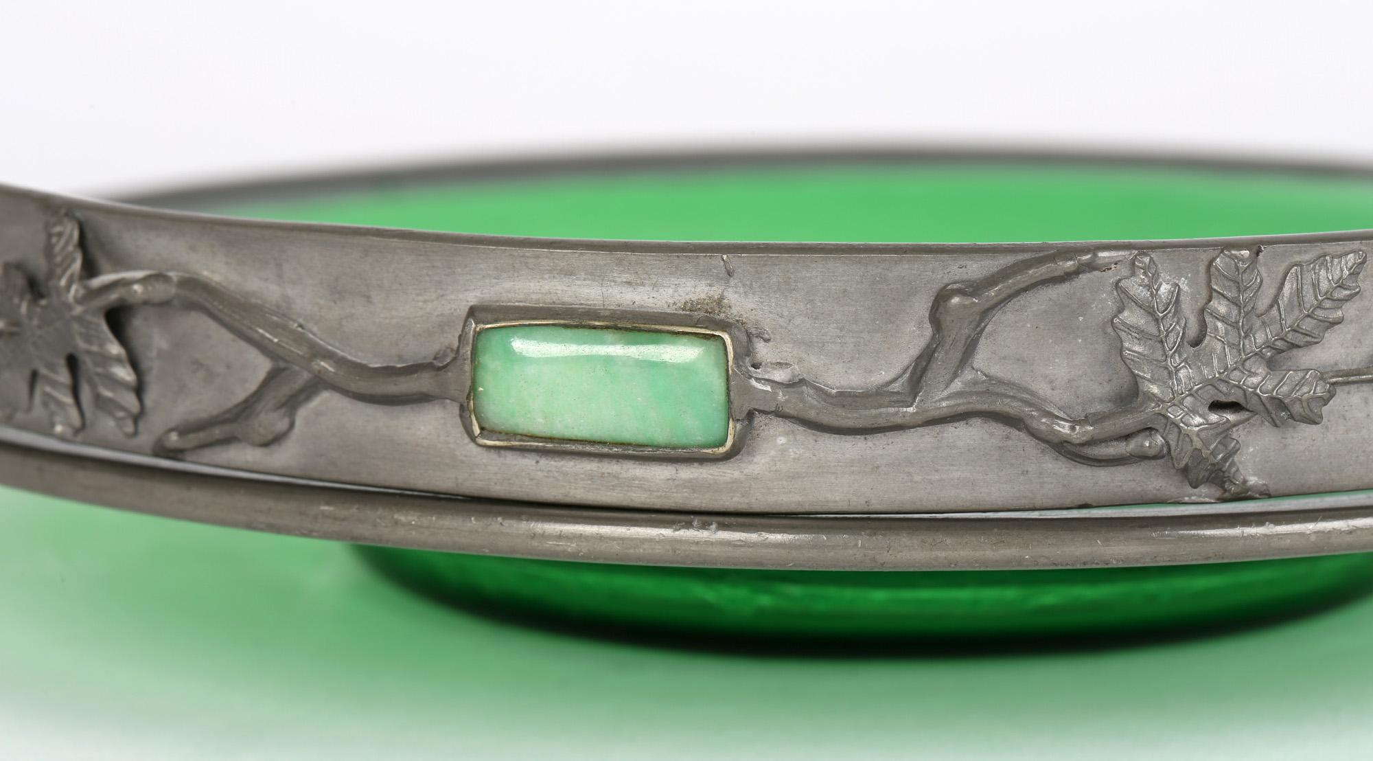 Inhabituel plat en verre vert monté en étain Arts & Crafts, l'anse pivotante incrustée de pierres précieuses polies, datant du début du 20e siècle. Ce plat de qualité finement fabriqué présente un plat arrondi en verre soufflé vert tacheté avec un