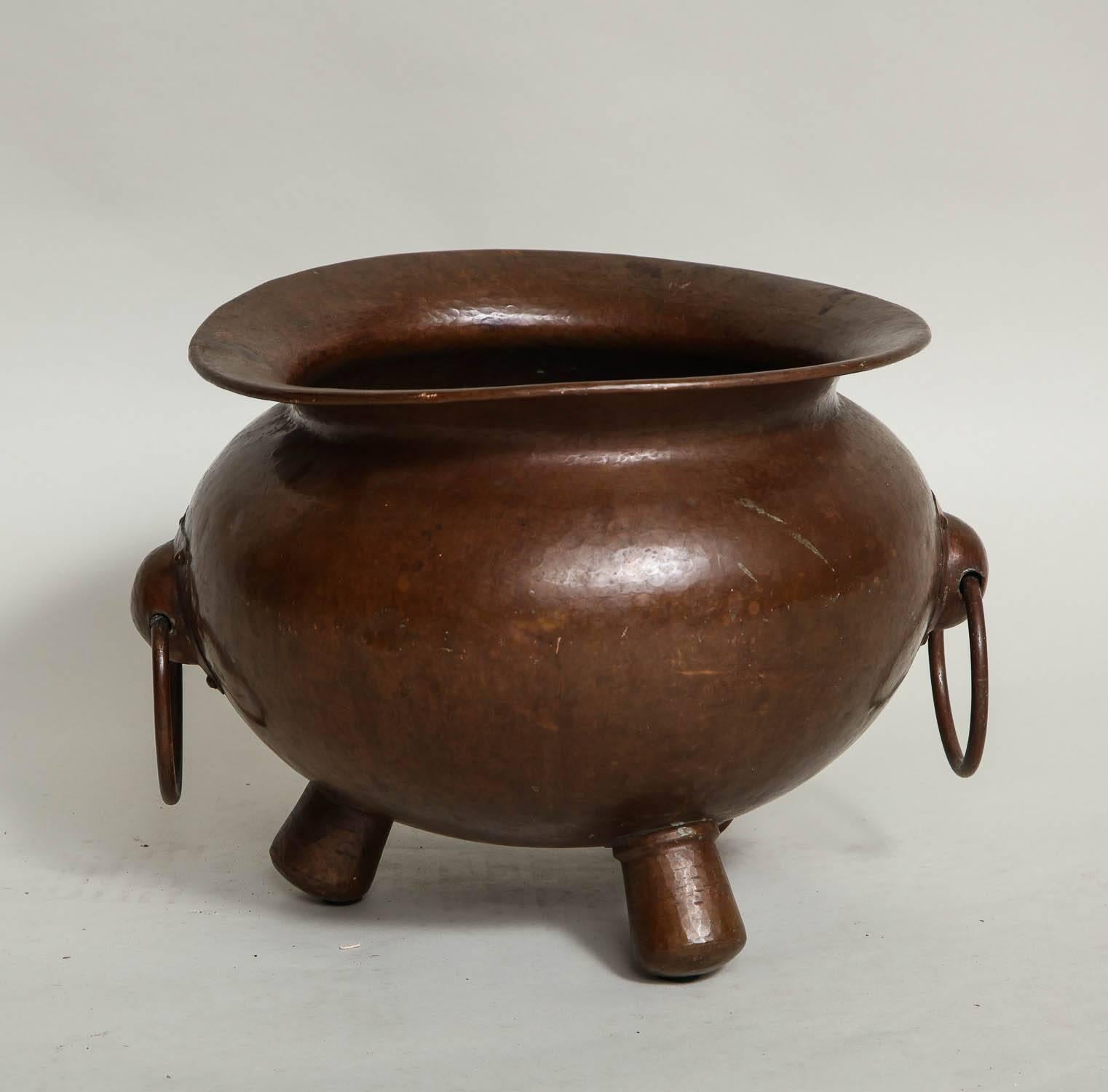 Fine early 20th century hammered copper cauldron form vessel, having generous rolled lip, swelled body with two applied handles and standing on stubby hollow feet, the whole with rich patination. Unsigned.
