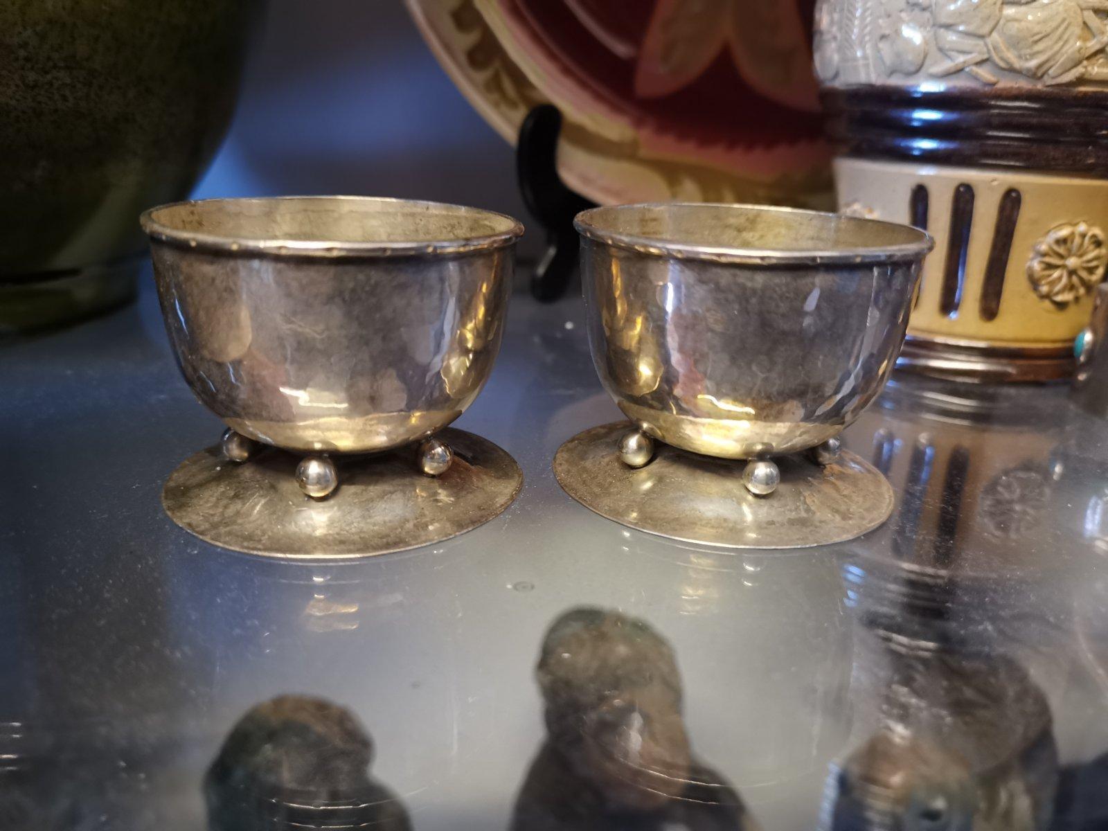 C R Ashbee for the guild of handicraft.
A rare pair of Arts & Crafts silver salt bowls with roll-over rims and dot decoration to the bowl edges stood on four ball feet on a flaring base foot.
Ashbee returned to this ball feet design on many
