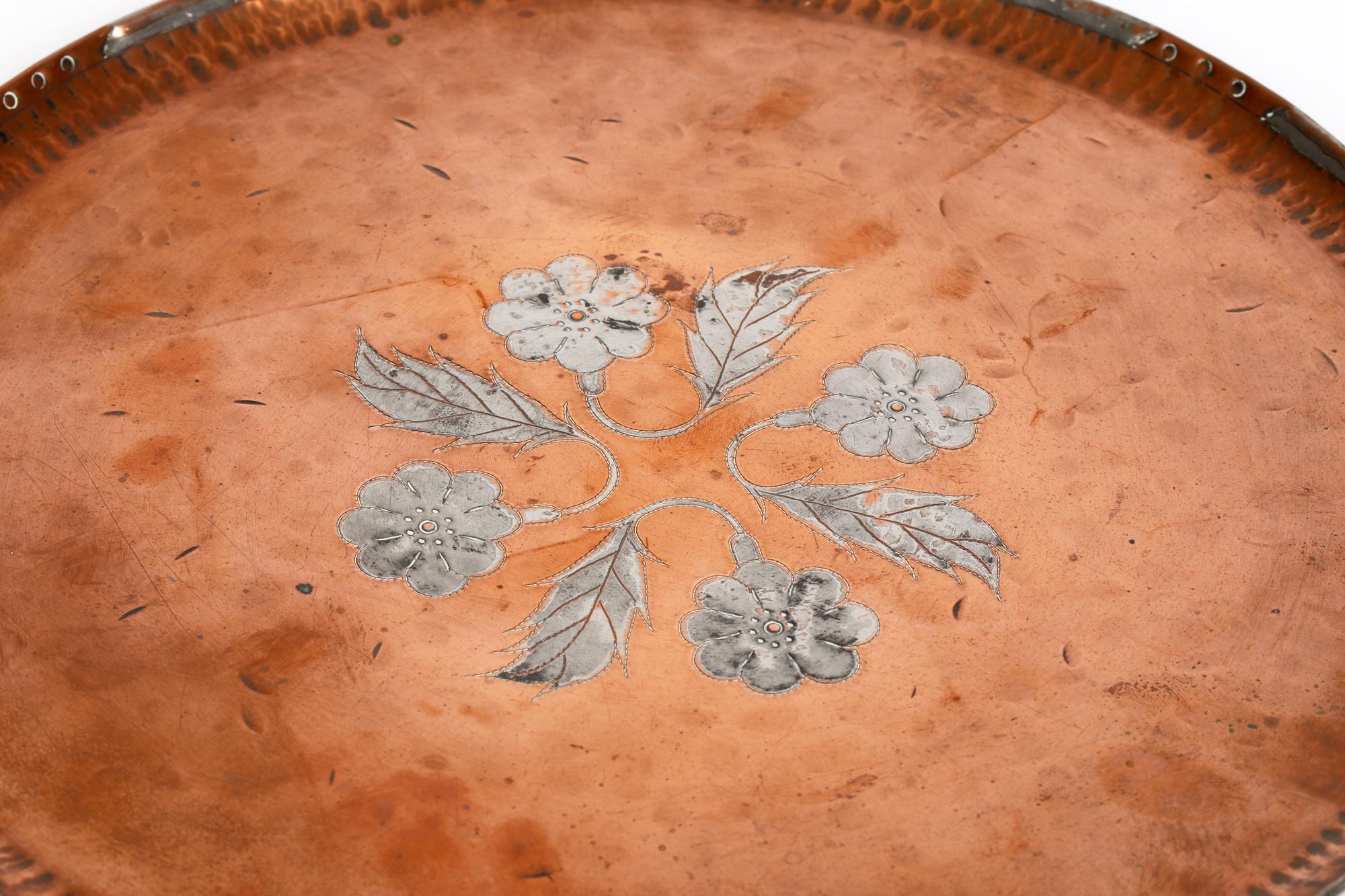 Arts & Crafts copper inlaid tray with pewter floral designs in the manner of Hugh Wallis and signed PG dating from around 1900. The rounded tray has a raised folded edge rim with a planished finish and with stud work and inlaid pewter designs. The