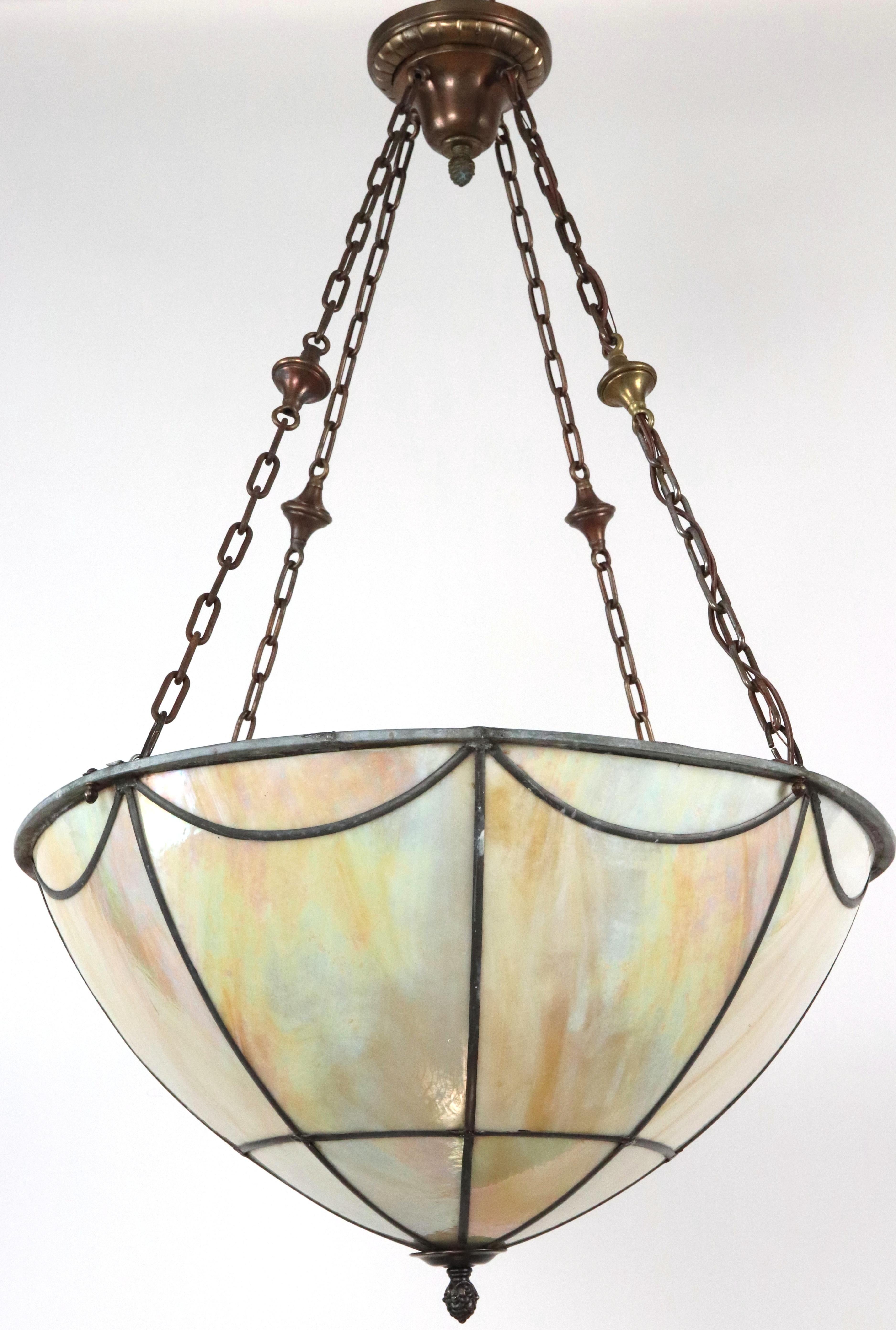 Lampe suspendue de style Arts & Crafts, avec des panneaux de verre irisé reliés entre eux par du plomb pour créer un motif géométrique. La chaîne est en acier plaqué laiton. Le reste de la quincaillerie est en laiton. Elle nécessite quatre ampoules