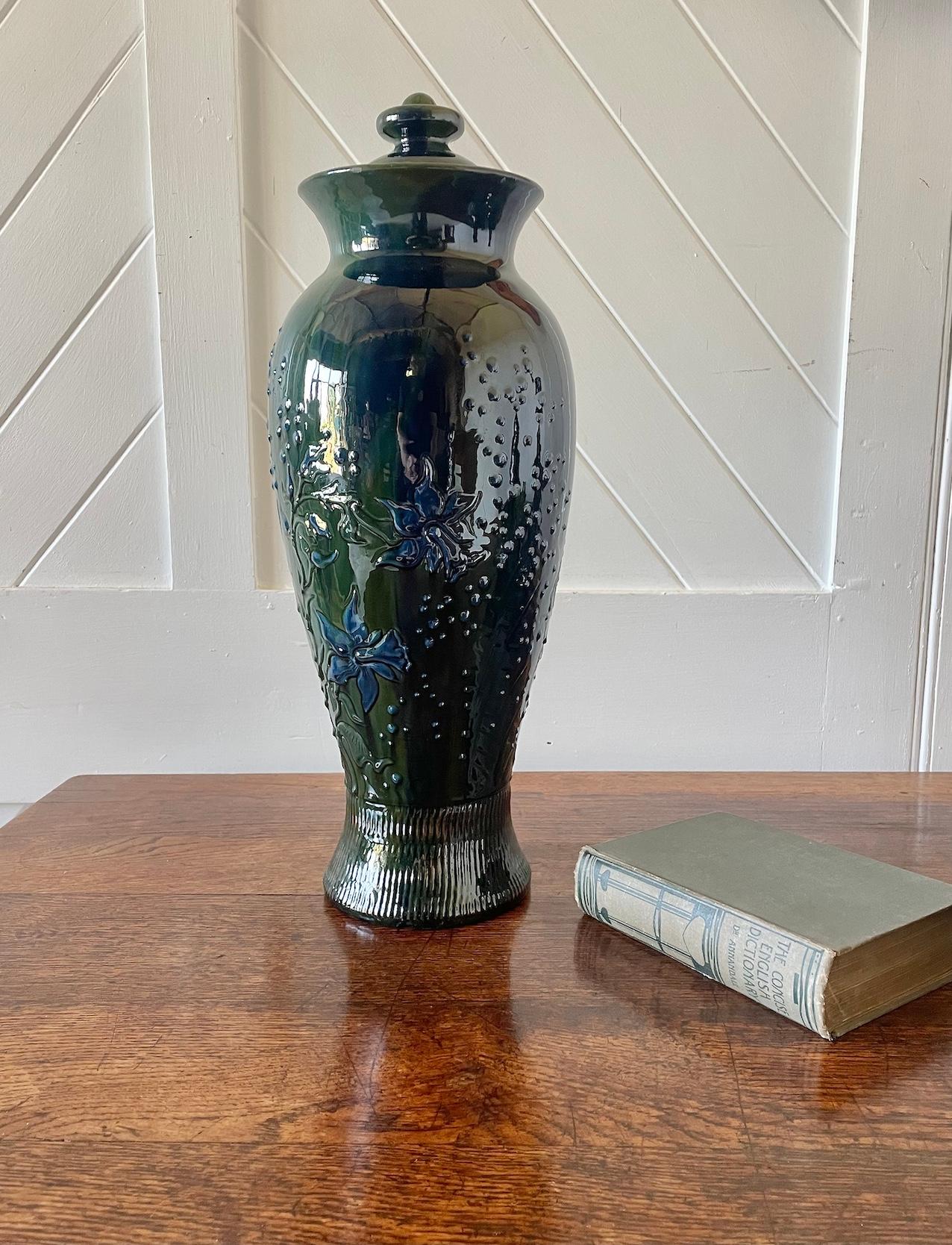 Arts & Crafts Sunflower Pottery große Vase mit Deckel 

In Grüntönen mit stilisierten blauen Narzissen 

Bleiglasiertes Steingut mit erhabenem Schlickerdekor

Gemaltes Elton's Zeichen

Elton's Ware

CIRCA 1910