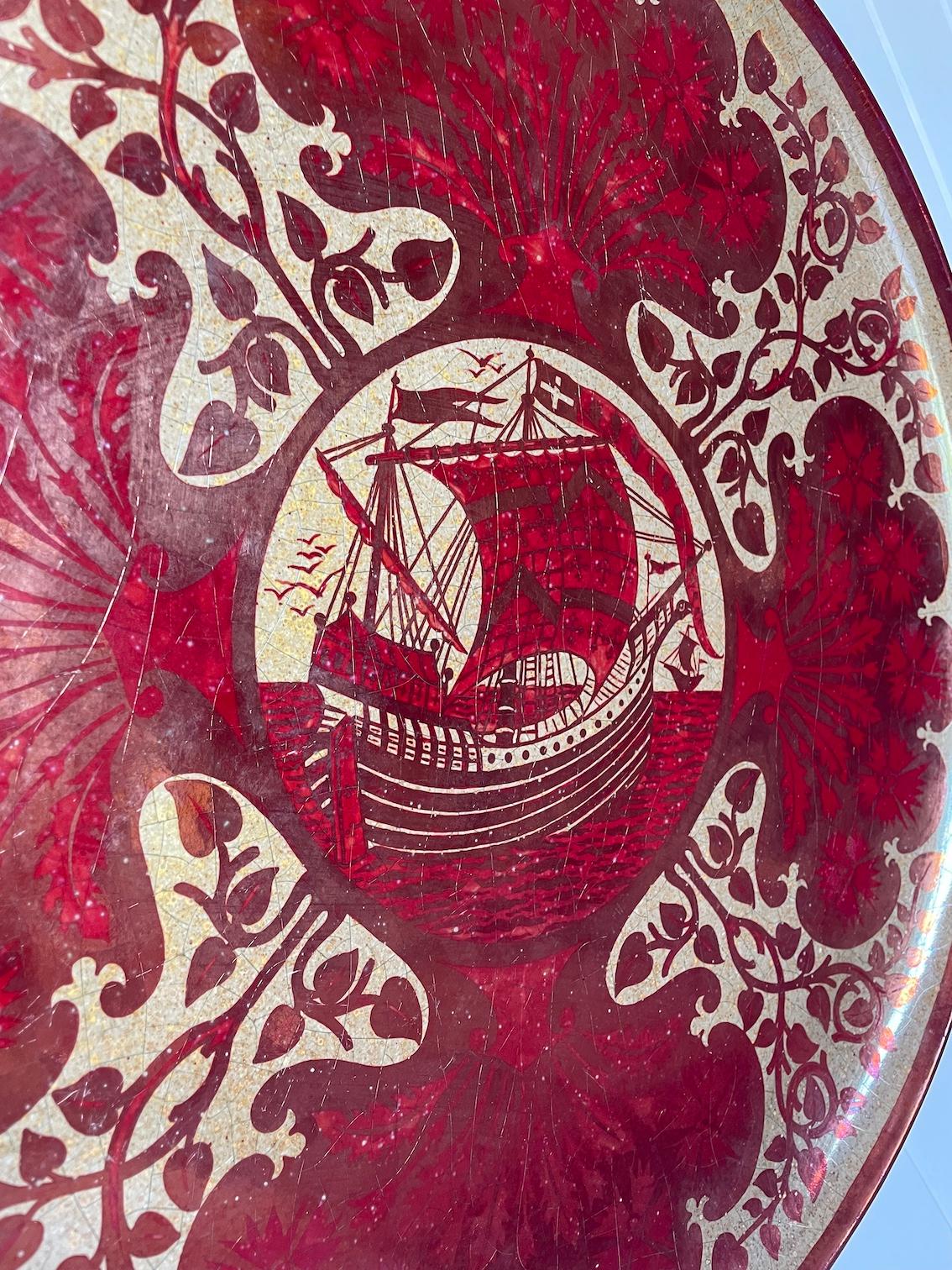 Arts & Crafts large Ruby lustre wall charger depicting a Galleon at sail 
surrounded by carnation flower panels and scrolling vines
Ruby and copper colouring on a cream background

Printed factory mark

Maw & Co

Maw & Co were one of the largest