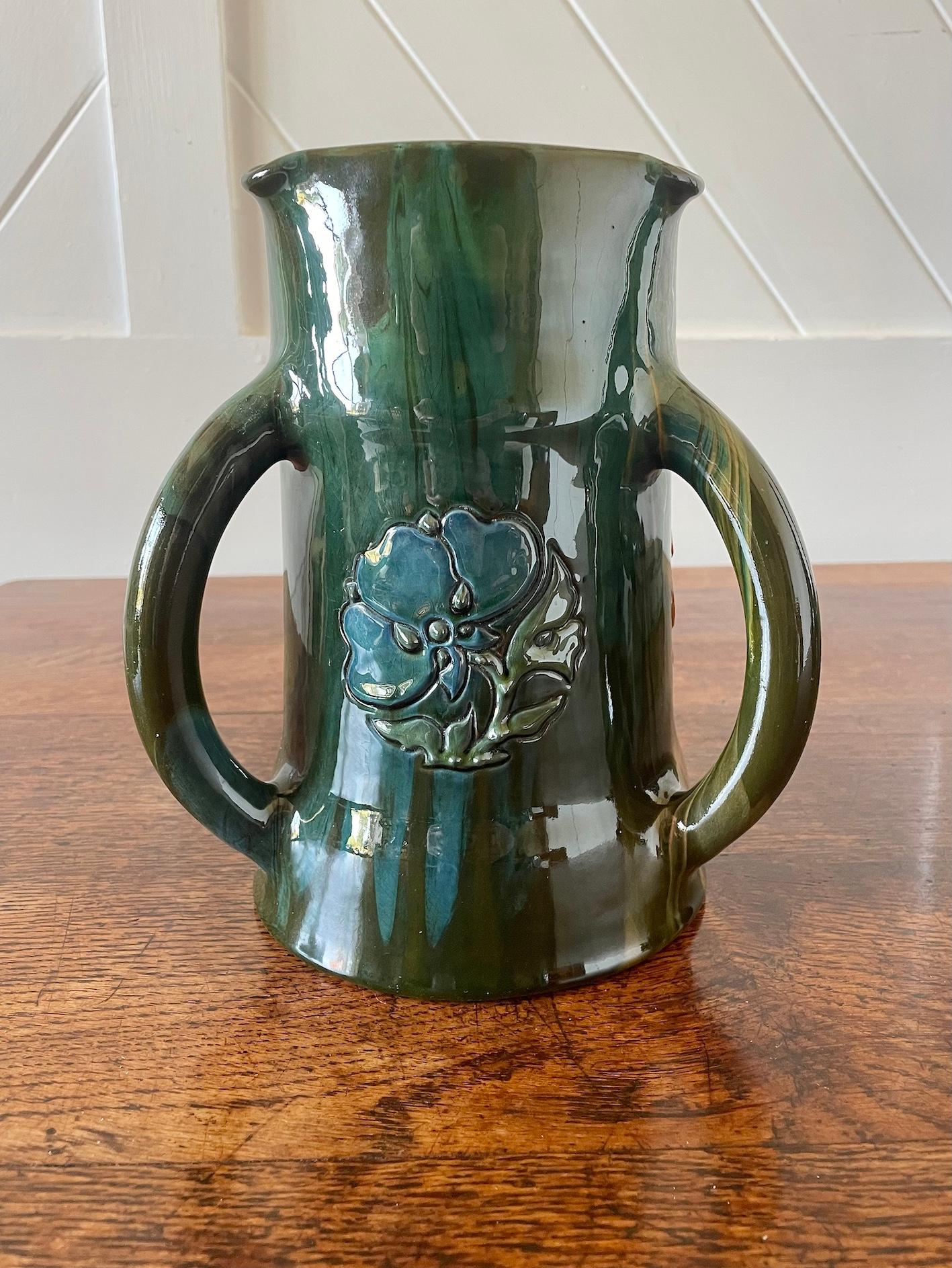 Arts & Crafts pottery 3 handled tyg with applied floral roundels

In shades of blues, greens and orange

Lead glazed earthenware with raised slip decoration

Painted Elton Mark

Elton Ware

Dated 1911
