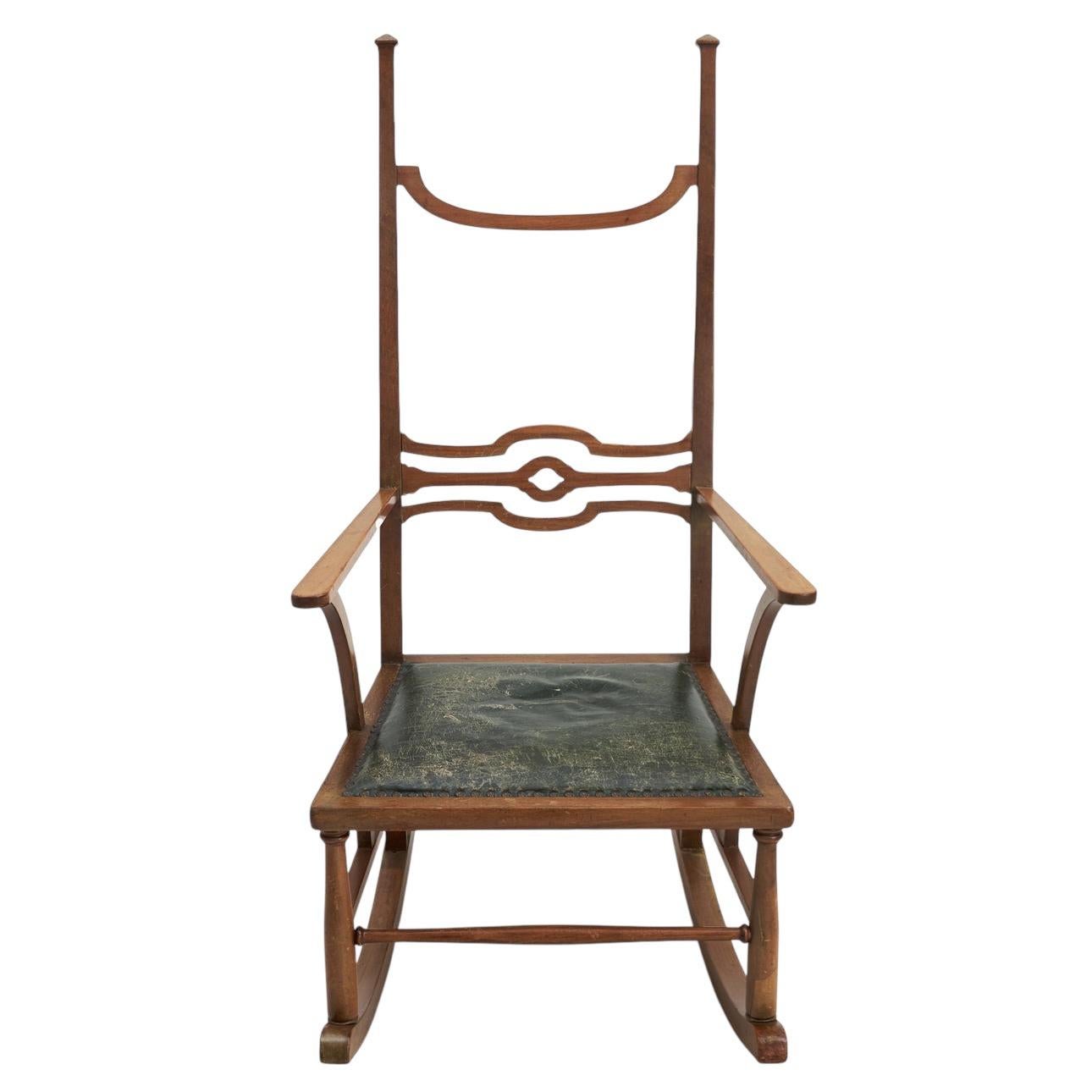 Step back in time with this exquisite early 20th-century rocking chair, an elegant representation of the Arts & Crafts movement. Crafted from rich mahogany wood, the chair features a tall, sculptural backrest with intricate cutout details,