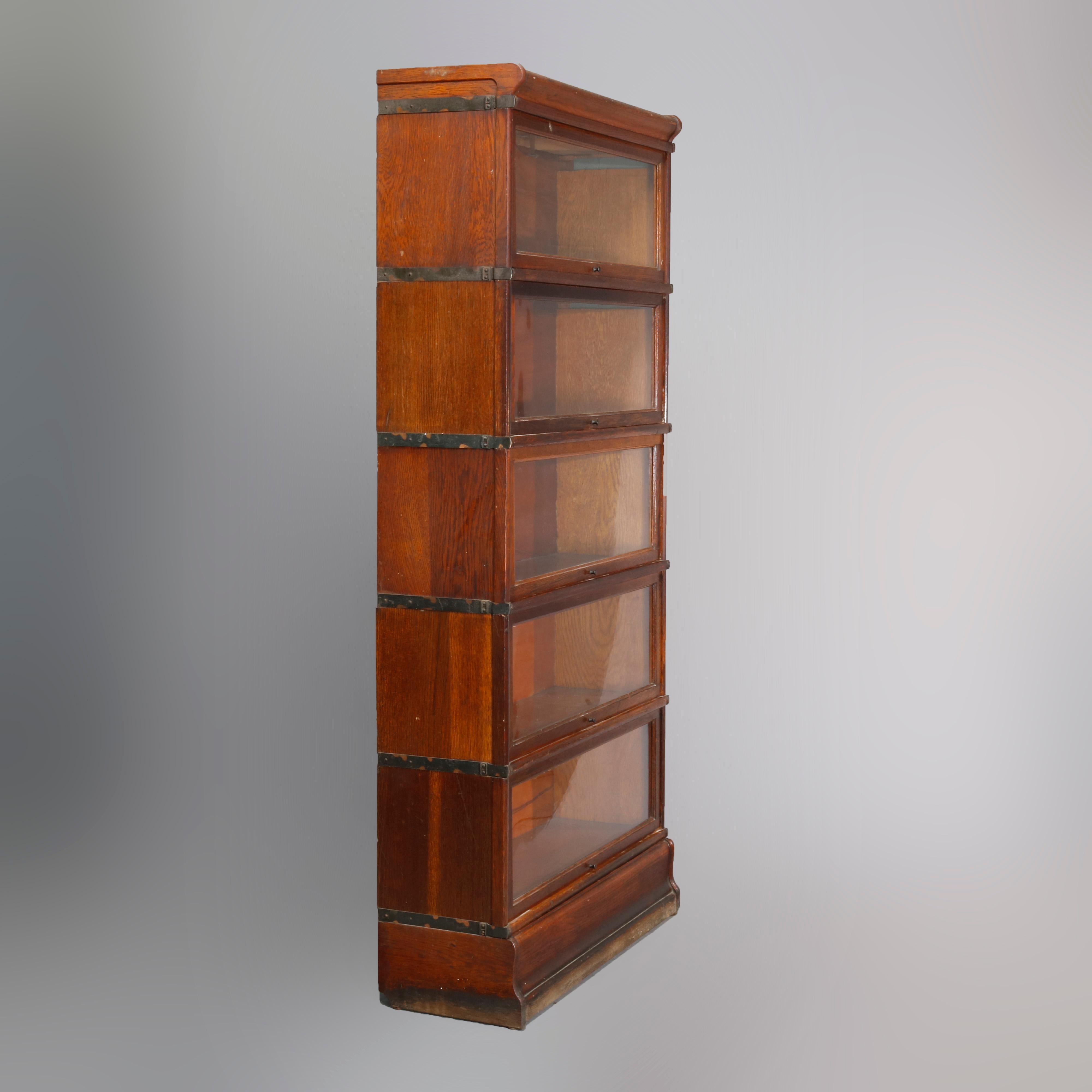 An Arts & Crafts sectional barrister bookcase by Globe-Wernicke offers quarter sawn oak construction with five stacks each having a pull-down glass door, raised on shaped base and surmounted by removable crown, original labels as photographed, circa