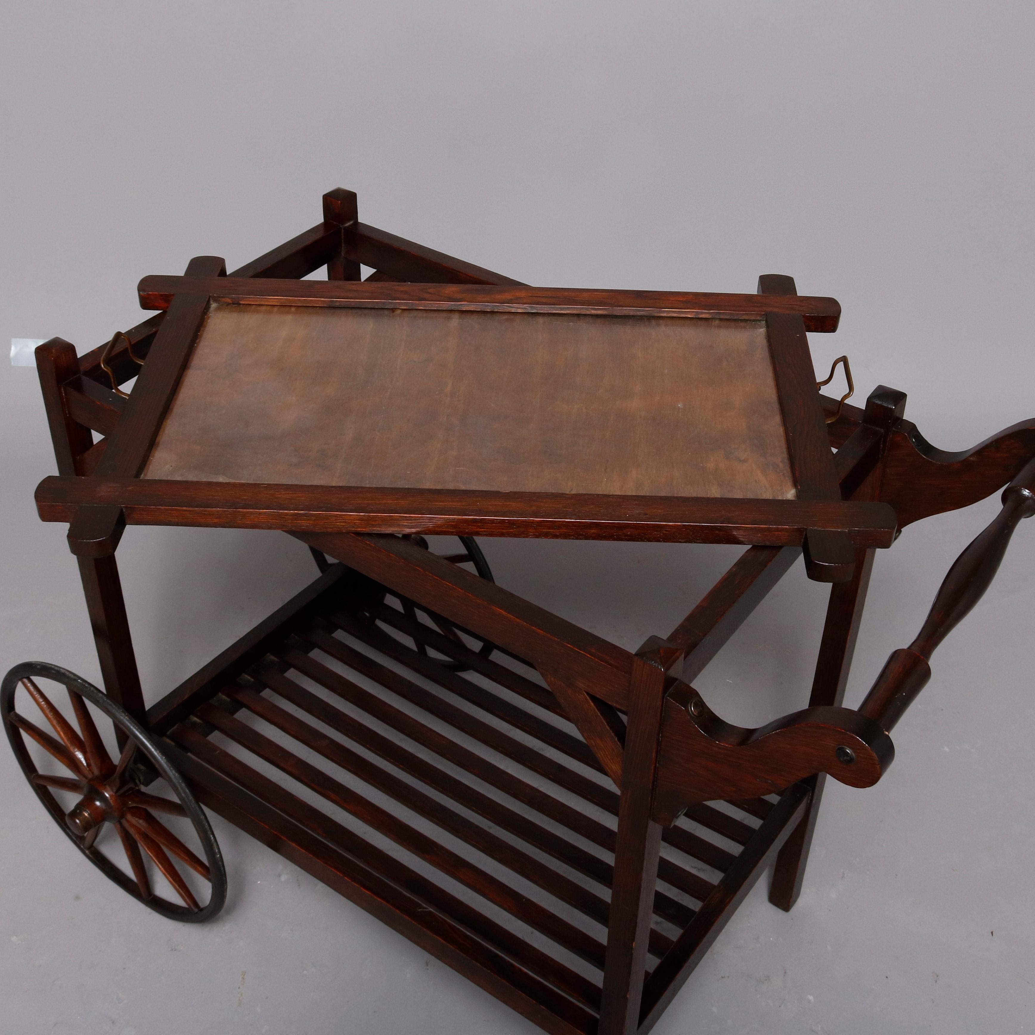 An Arts & Crafts Mission oak stickley brothers school tea cart offers upper removable serving tray, shaped handle, lower slat shelf and oversized wheels, circa 1910.

Measures - 30