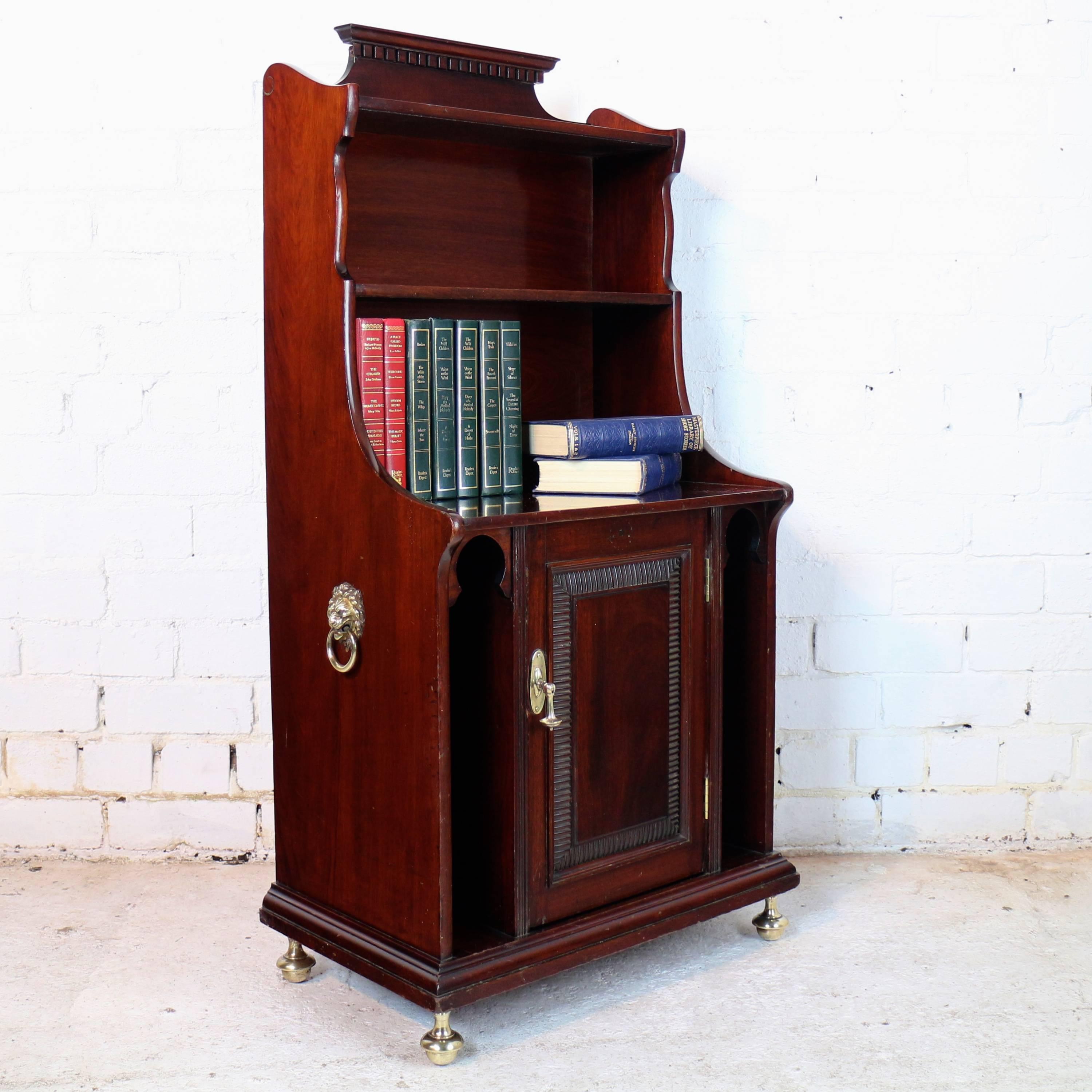 An Arts & Crafts mahogany waterfall bookcase cabinet by Shapland & Petter of Barnstaple, featuring Moorish inspired mihrab shaped tall recesses, ribbed molding to the door and brass lion mask carry handles to the sides it has a molded dentil cornice
