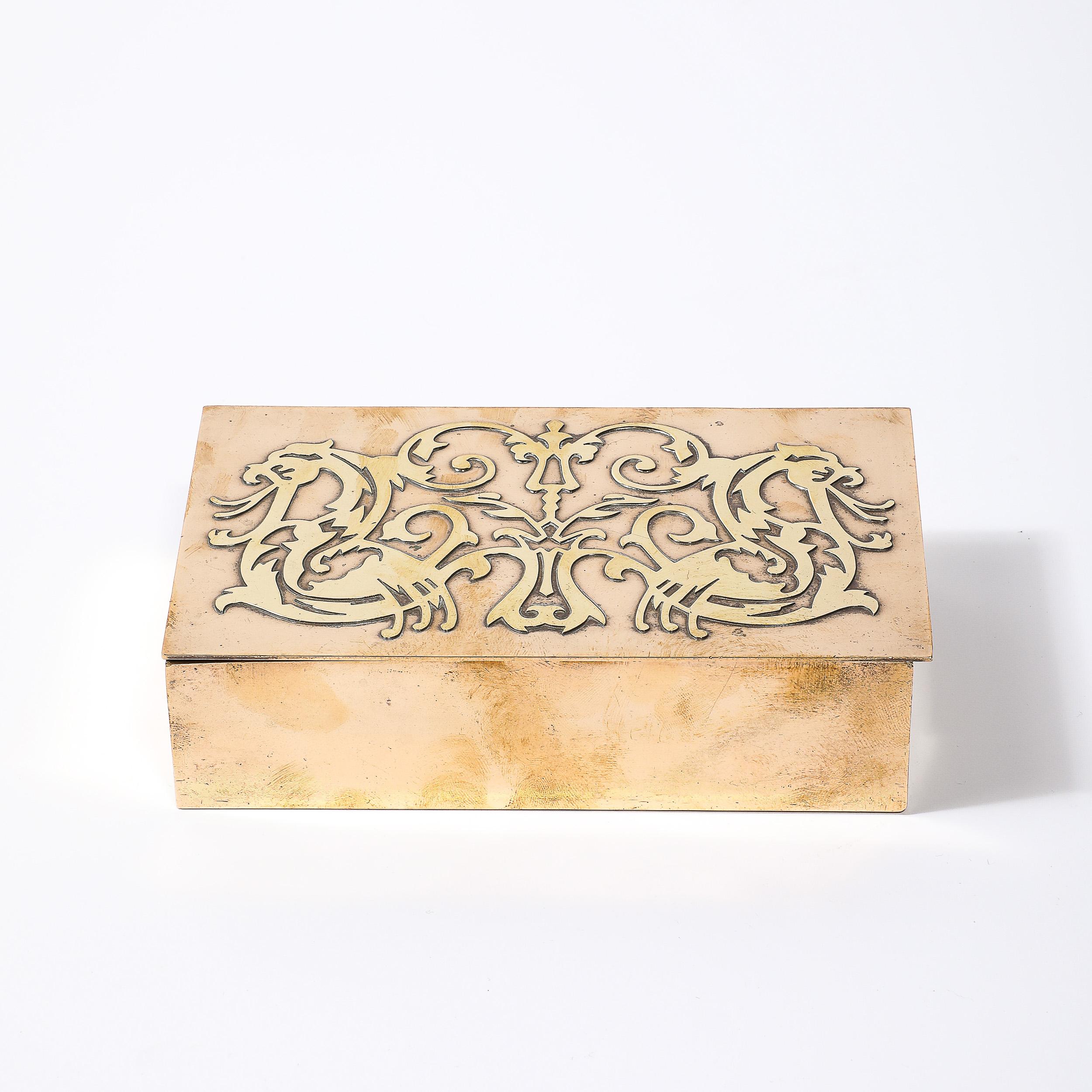 Esta caja de bronce y latón forrada de nogal del movimiento Arts and Crafts, brillantemente detallada, con detalles heráldicos y firmada con el escudo de plata, procede de Estados Unidos de principios del siglo XX. Presenta un complejo diseño