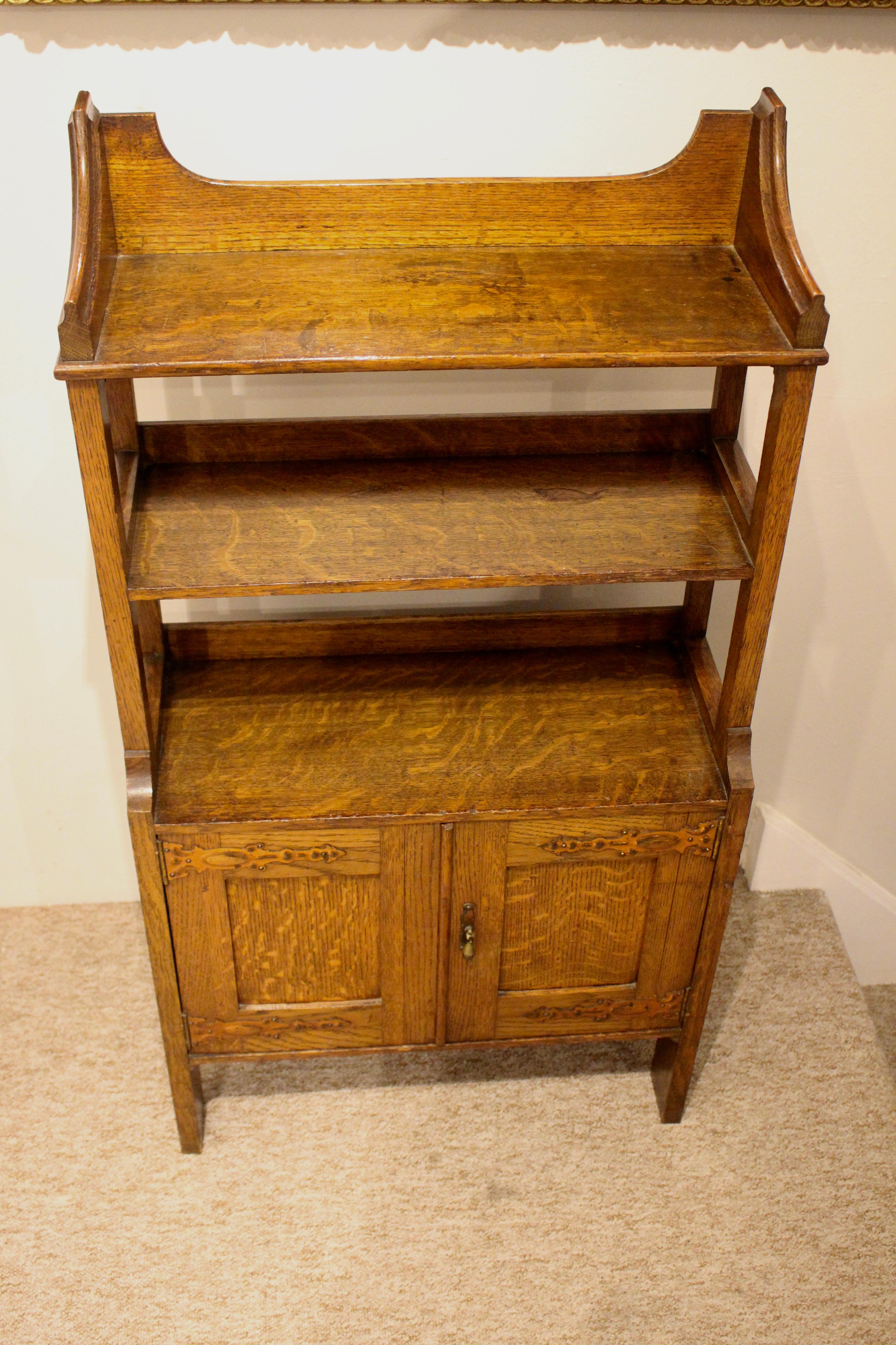 A nicely proportioned Arts & Crafts oak bookcase. Having three shelves above a double cupboard. The upper shelf with interesting quadrant detail. The cupboard doors with copper strap work and a pretty solid brass drop handle. The whole standing on