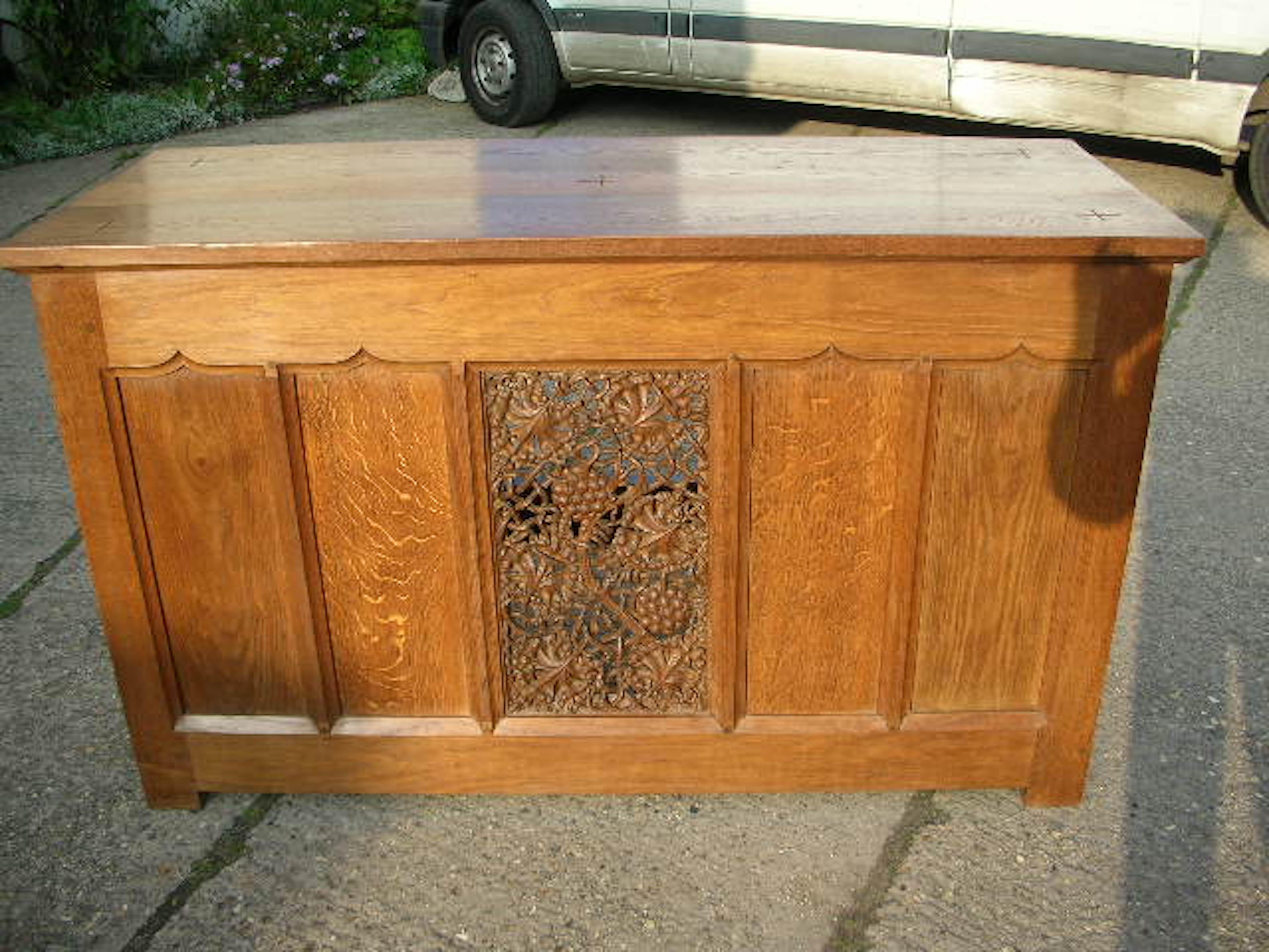 Arthur Simpson of Kendal attributed. 
A fine quality Arts and Crafts Gothic Revival style oak Altar, serving or buffet table with a finely carved center panel of fruiting vines, flanked by fielded panels with subtly arched details to the top, and