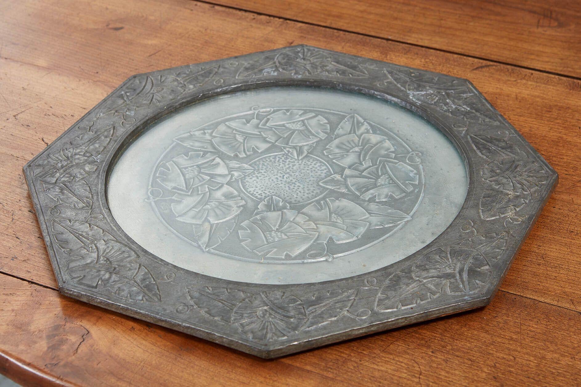 An Arts & Crafts octagonal wall tray in two toned pewter with circular glass center decorated around rim and under glass with vine and leaf motif. Original glass and backboard. English, circa 1900.