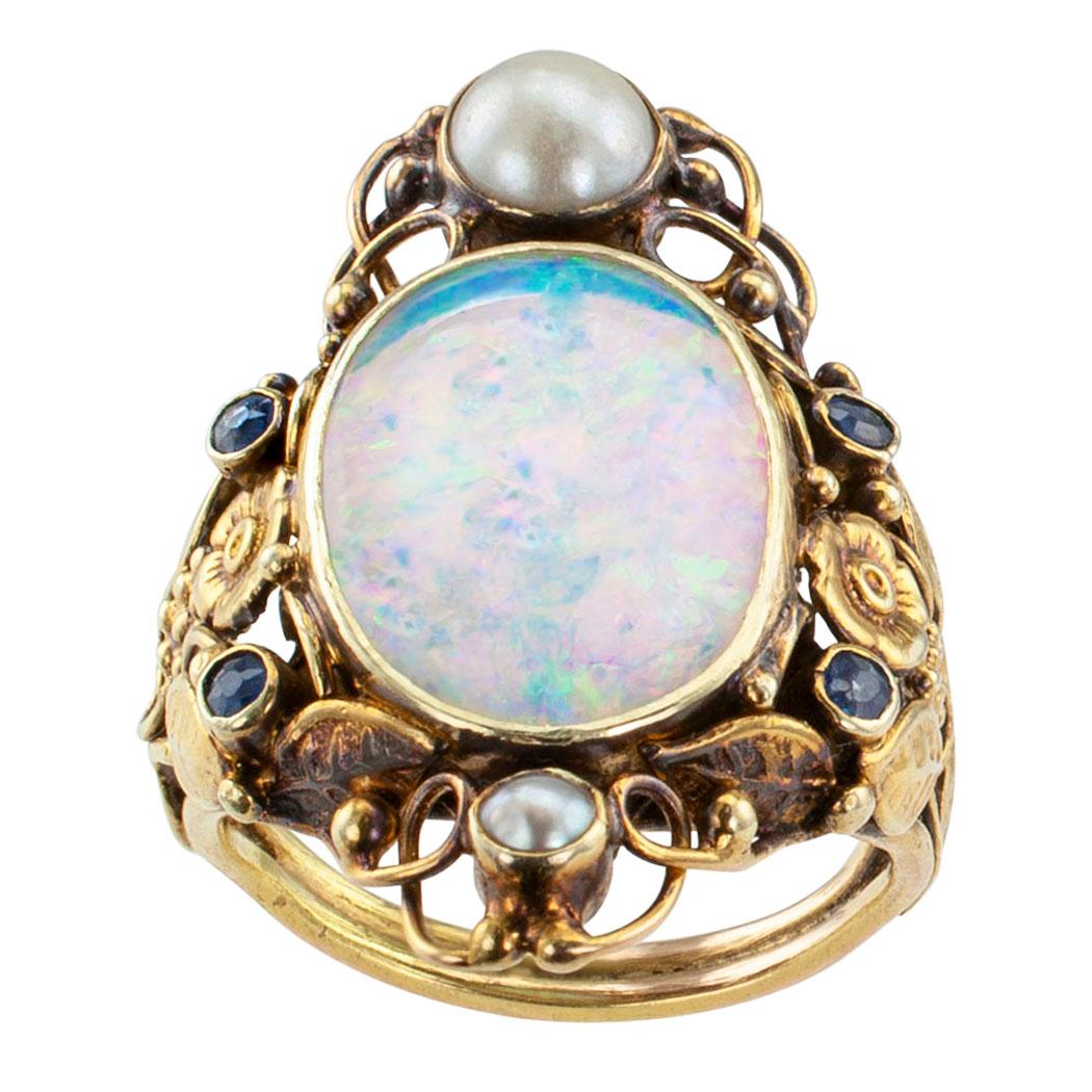 Arts and Crafts opal pearl and sapphire gold ring circa 1900. Showcasing a bezel-set opal enveloped by an open work garland of flowers balanced between two pearls and accented with four smaller round sapphires, to the gallery and shank, handcrafted