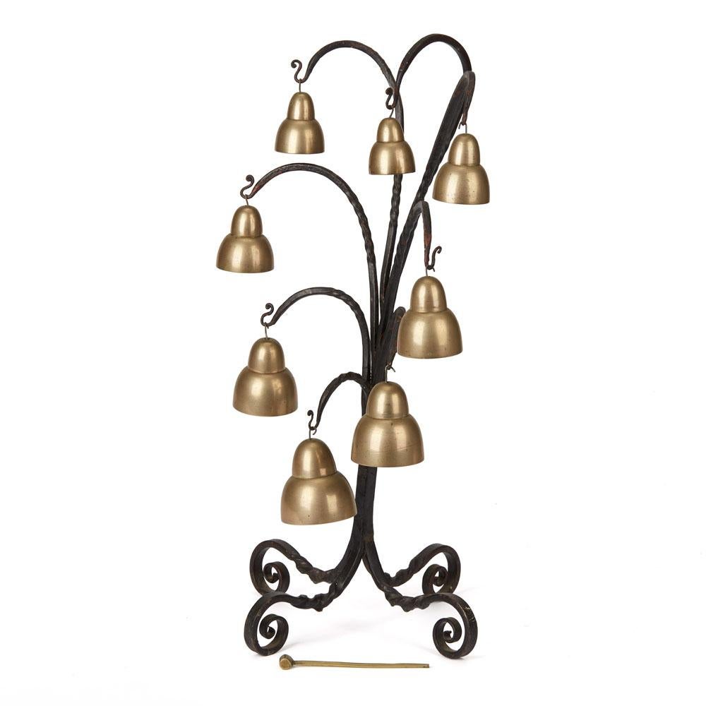 An Arts & Crafts peal gong with eight brass bells mounted on a wrought iron stand with a small brass hammer and probably retailed by Liberty & Co. The eight bells are of graduated size and each is sized so as to play a sequence of eight tones, one