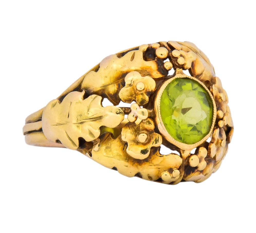 Centering a round cut peridot weighing approximately 1.20 carat total, transparent and bright yellowish-green in color

Bezel set in a millegrain bezel surrounded by stylized polished gold wildflowers and oak leaves

Completed by a ridged
