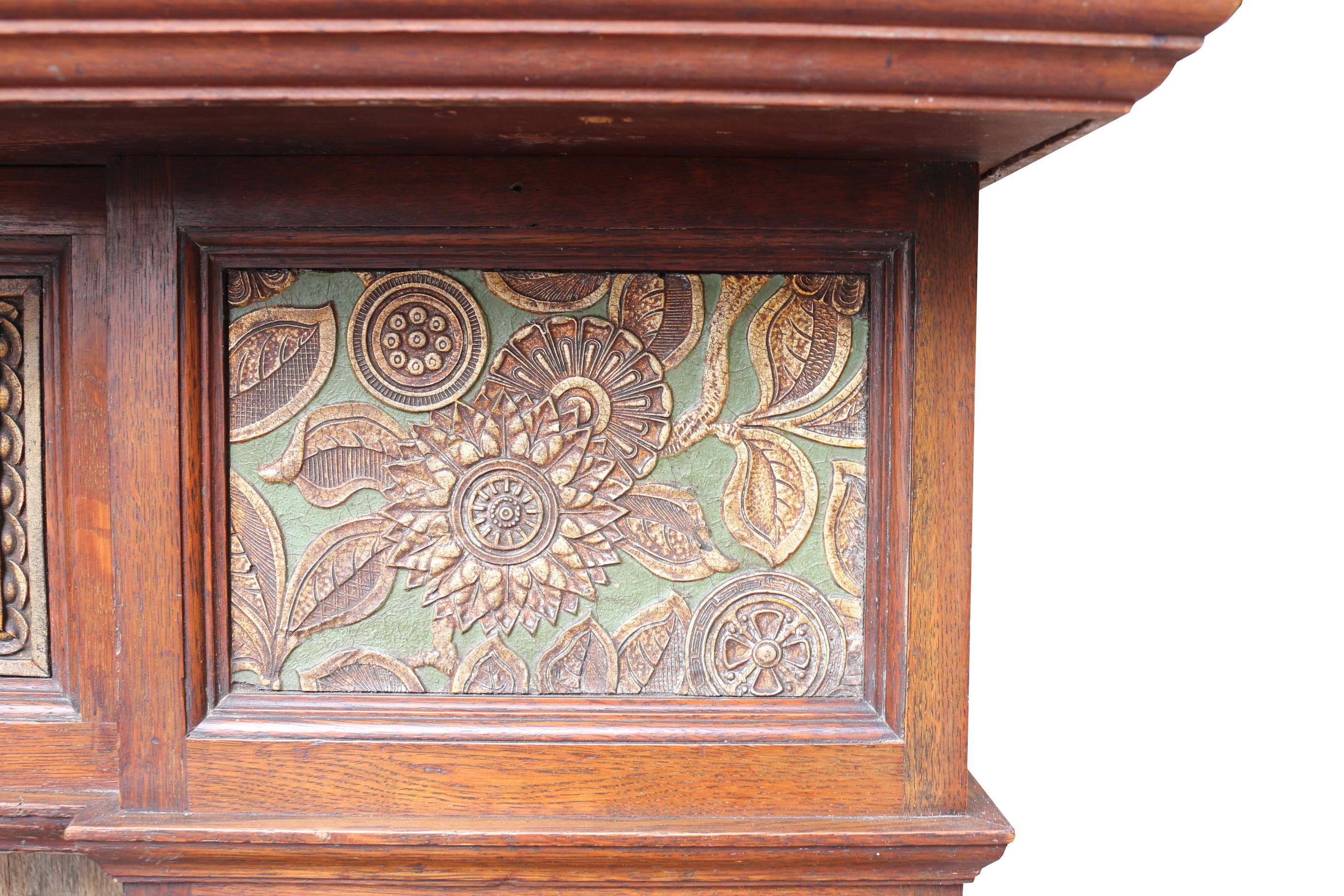 An original Arts & Crafts period oak fire surround with mirrored over mantle. The panels are a form of linoleum composite. Decorated in a green and gold scheme.

Measures: Height 220 cm
Width 166 cm
Depth 29 cm
Opening height 104 cm
Opening
