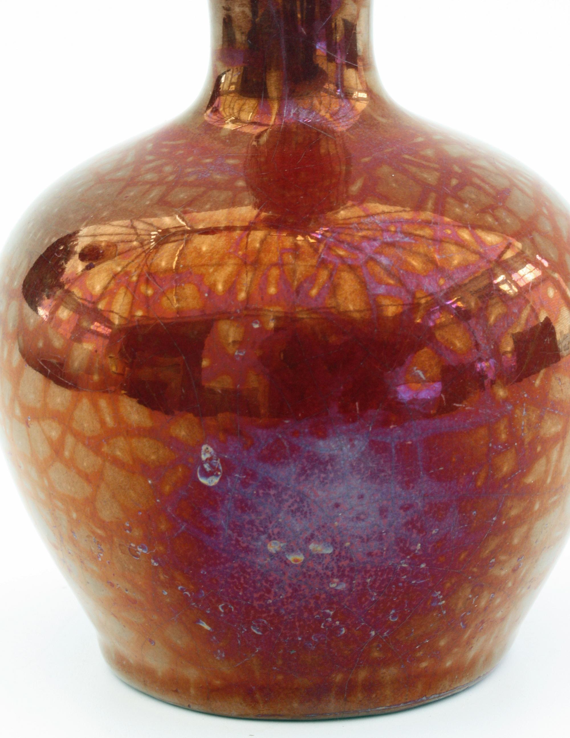 A stylish and lightly potted Arts & Crafts red luster glazed art pottery vase decorated with a spider web design dating from circa 1900. The small rounded bulbous shaped vase has a narrow trumpet shaped neck and is finished in beautiful red luster
