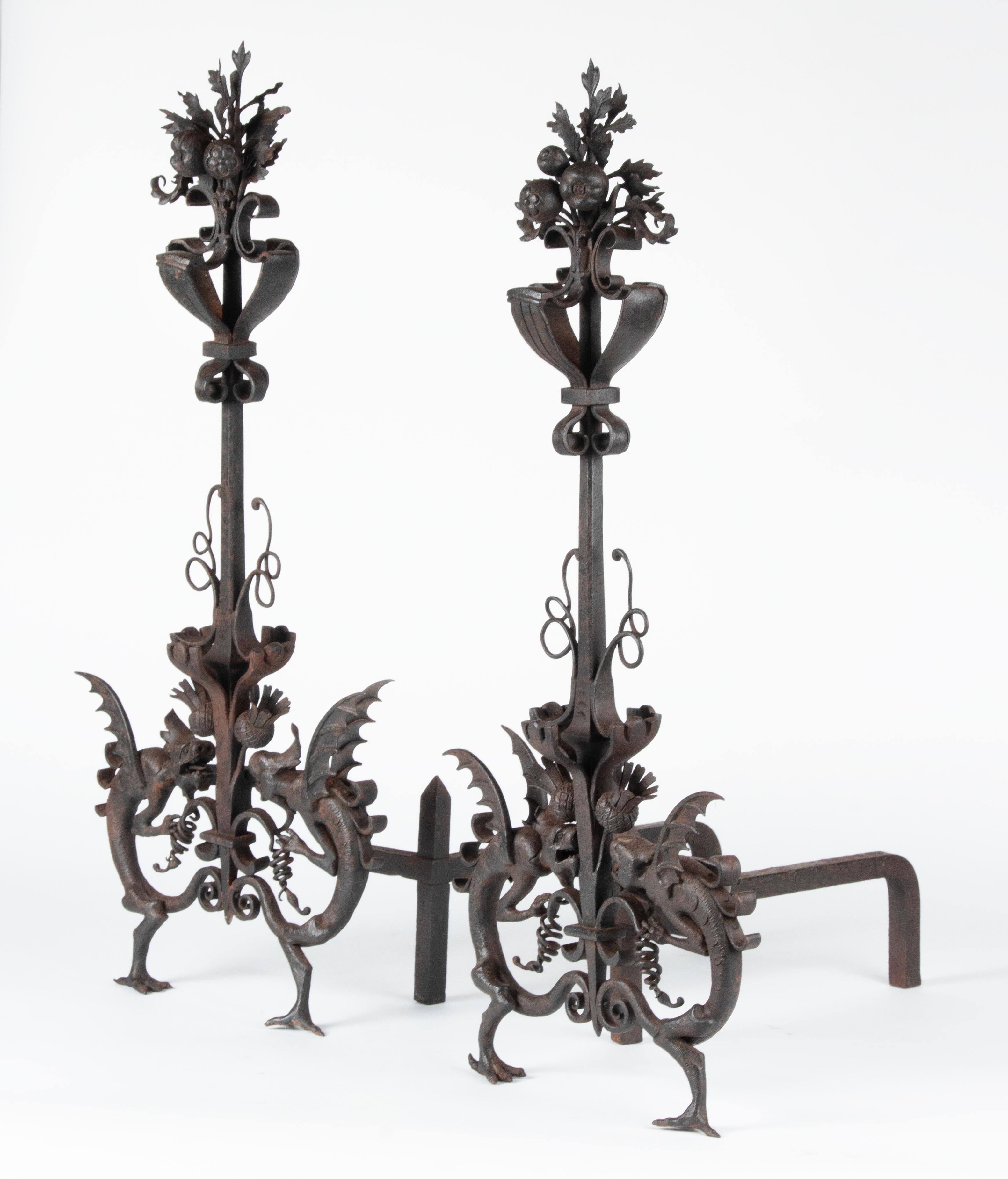 A pair of extra-tall handcrafted wrought iron and cast iron andirons in Samuel Yellin style, in the Arts & Crafts spirit. Partly hand-wrought and partly cast iron. With flanking dragons resting on his feet. At the top fruit with leaves. Excellence