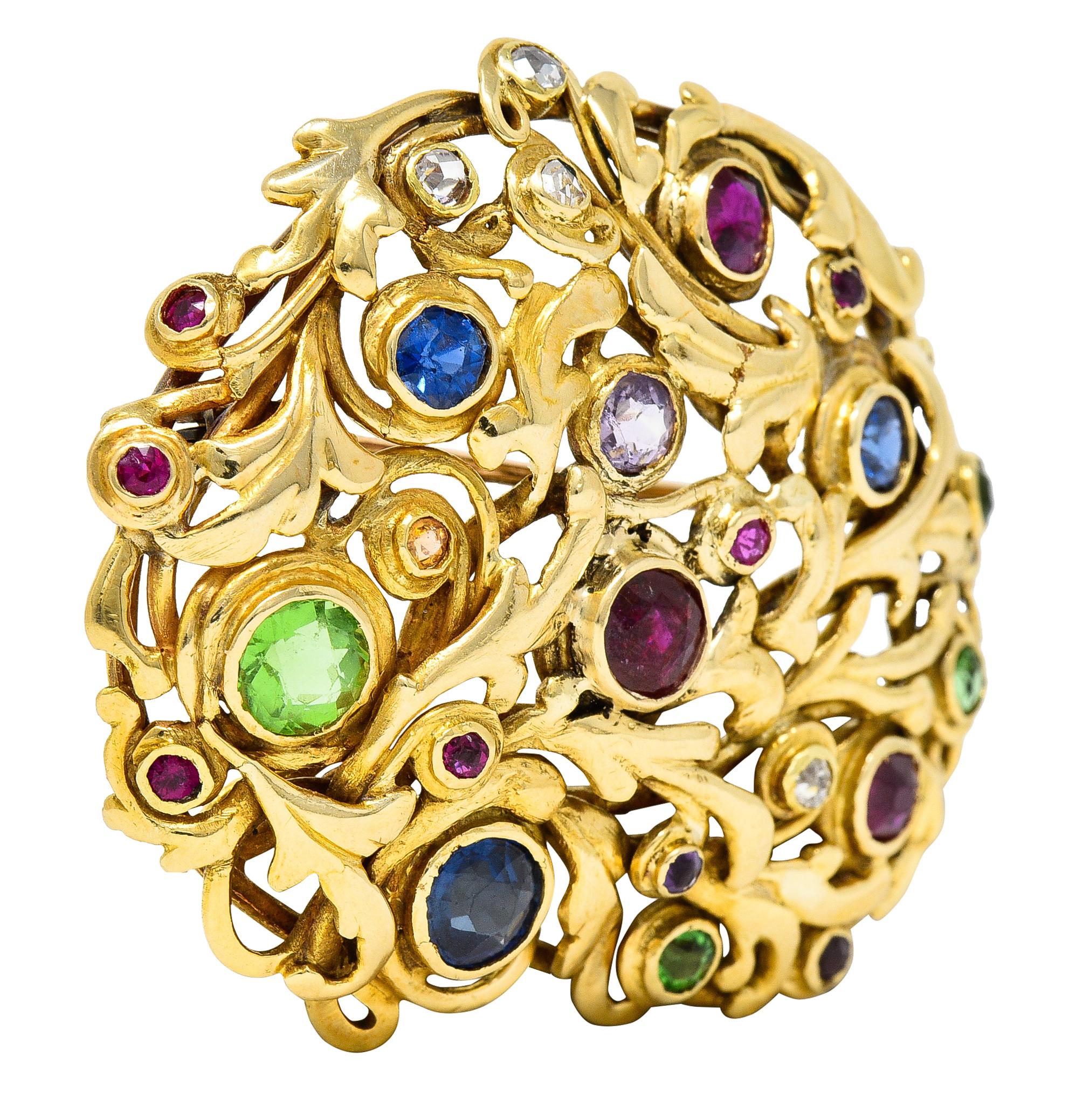 Substantial pendant brooch is designed as stylized foliate undulating and twisting together. Bezel set intermittently by round and cushion cut gemstones. Featuring blue sapphire, red ruby, green garnet, light purple amethyst, rose cut diamonds, and