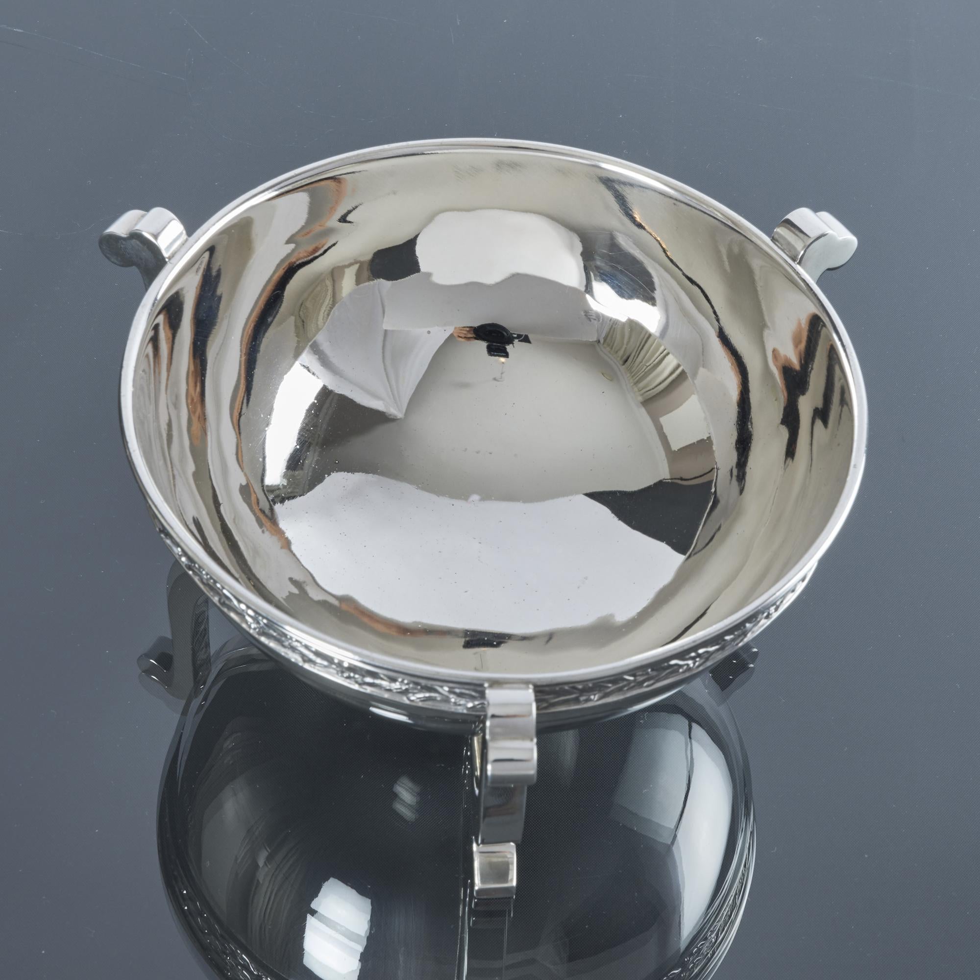 Cuenco de plata antigua de estilo Arts & Crafts montado sobre tres soportes en forma de criaturas estilizadas. El borde del cuenco está bellamente bordeado con una banda aplicada de decoración de hojas de laurel alrededor del borde.

Peso: 260 g