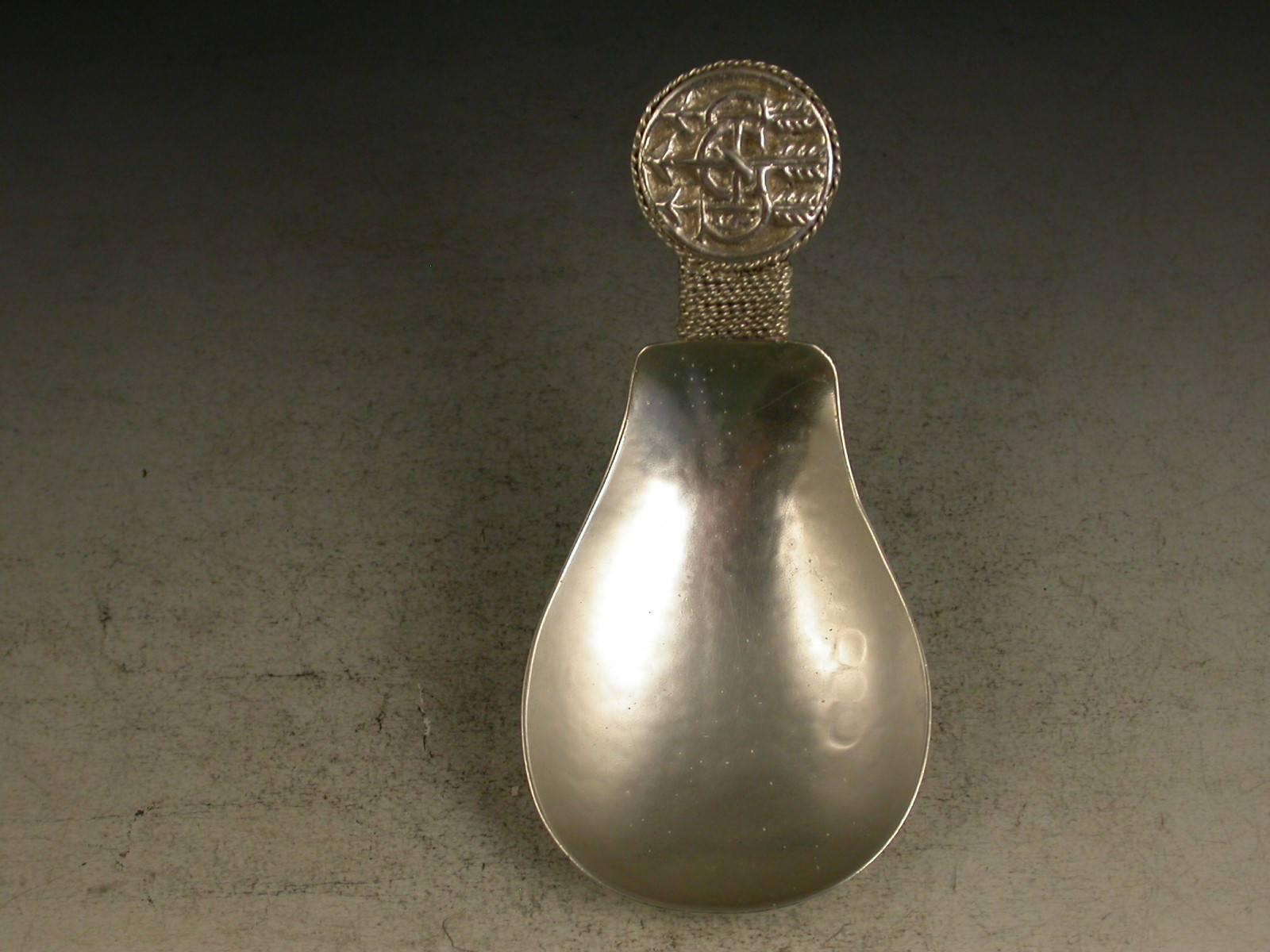 A fine early 20th century 'Arts & Crafts' cast silver caddy spoon with hammered pear shaped bowl, the disc shaped terminal with rope twist border chased with inter-twinned initials 'GS' pierced by three arrows.

Designed by Edward Spencer for the
