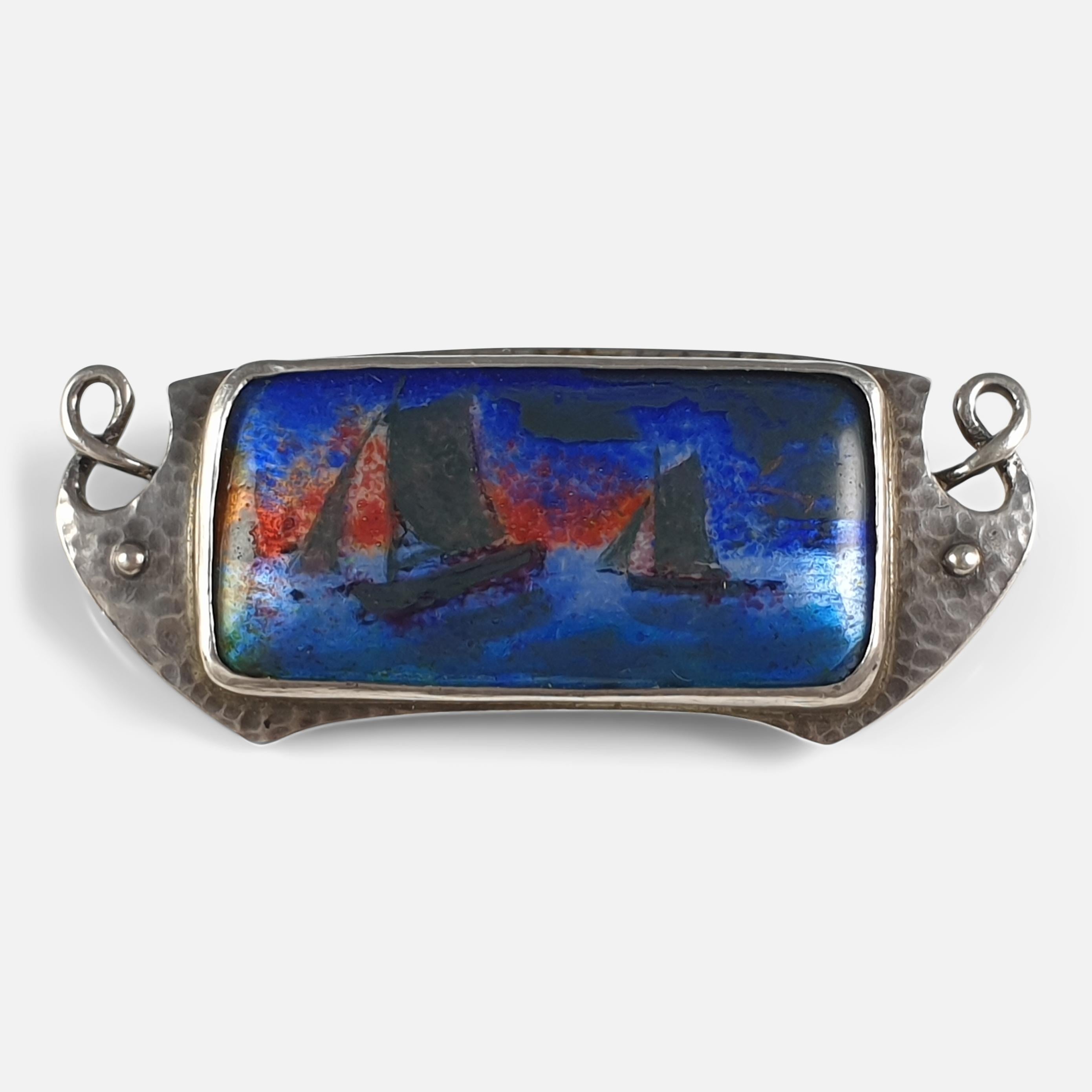 An Arts & Crafts spot-beaten silver and enamel plaque brooch by Murrle Bennett & Co, circa 1910. The brooch is set with an enamel plaque depicting sailing boats (possibly by Charles Fleetwood Varley), within a hammered silver surround. 

Stamped