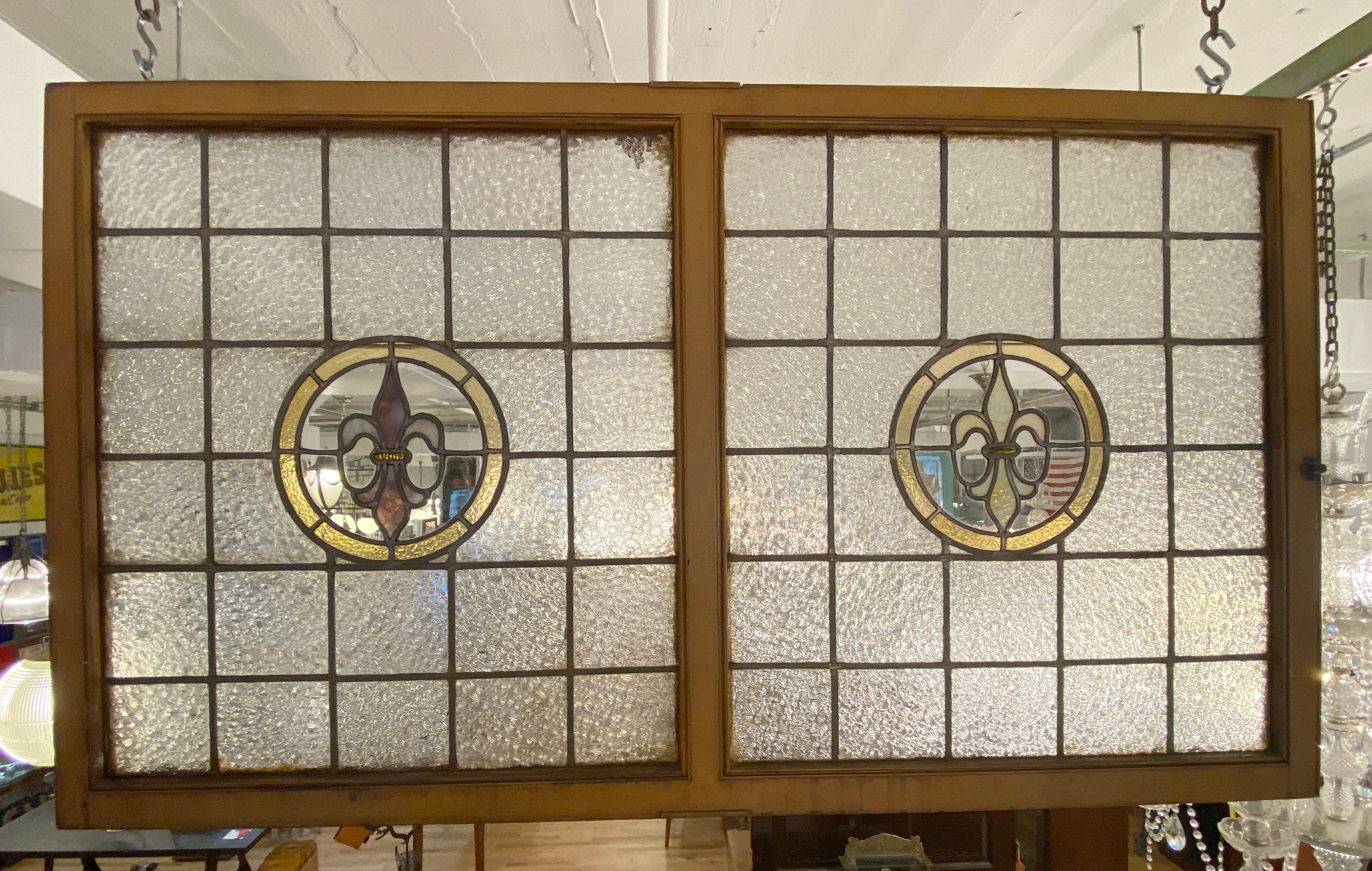 This antique double stained leaded glass window once graced the interior of the Grand Prospect Hall in Brooklyn, NY. It features two sides each with clear Florentine patterned square glass panels and the center has a yellow circle around an