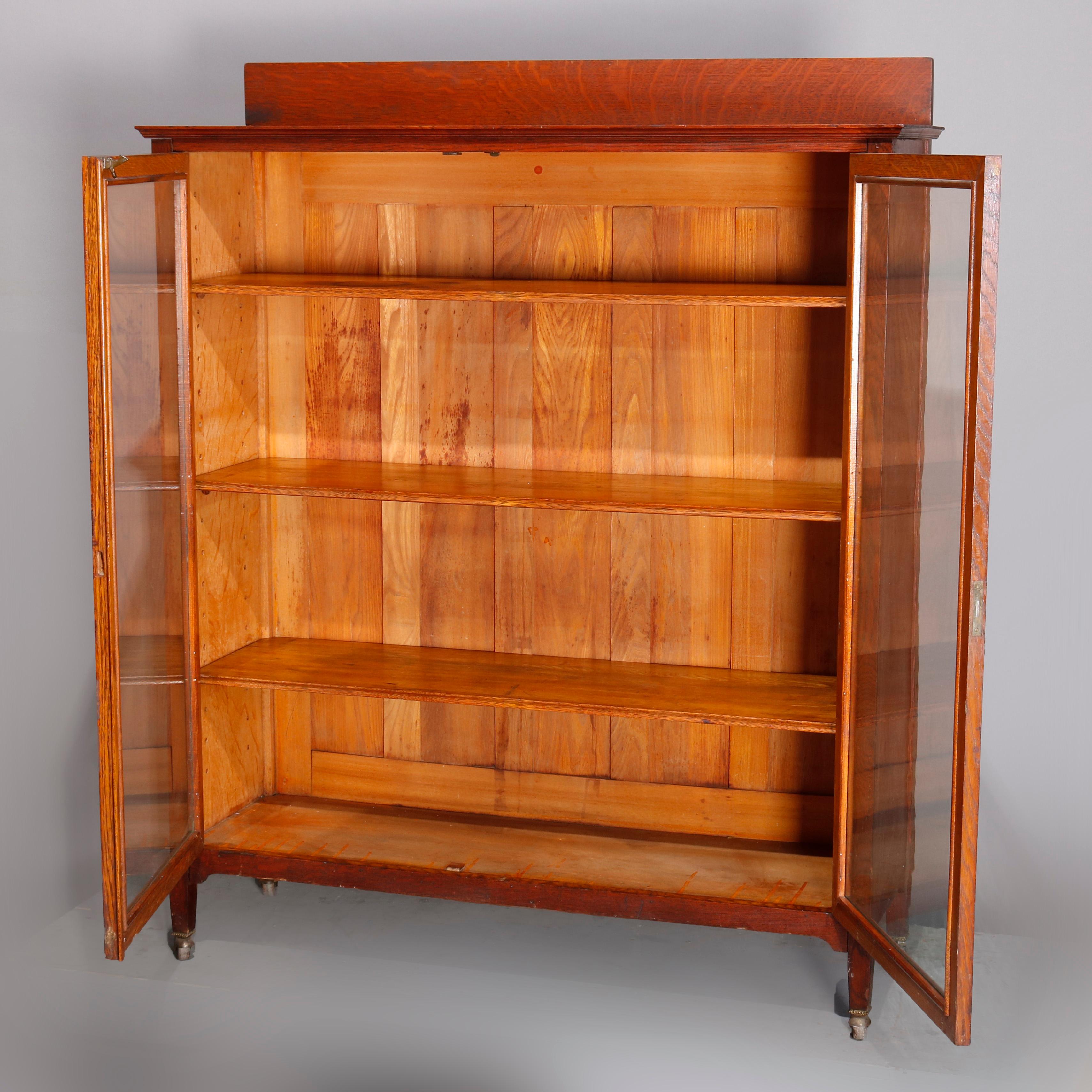 An antique Arts & Crafts Stickley School mission oak bookcase offers quarter sawn oak construction with backsplash surmounting double glass door case having adjustable shelved interior, raised on straight and square legs, circa 1910

Measures: