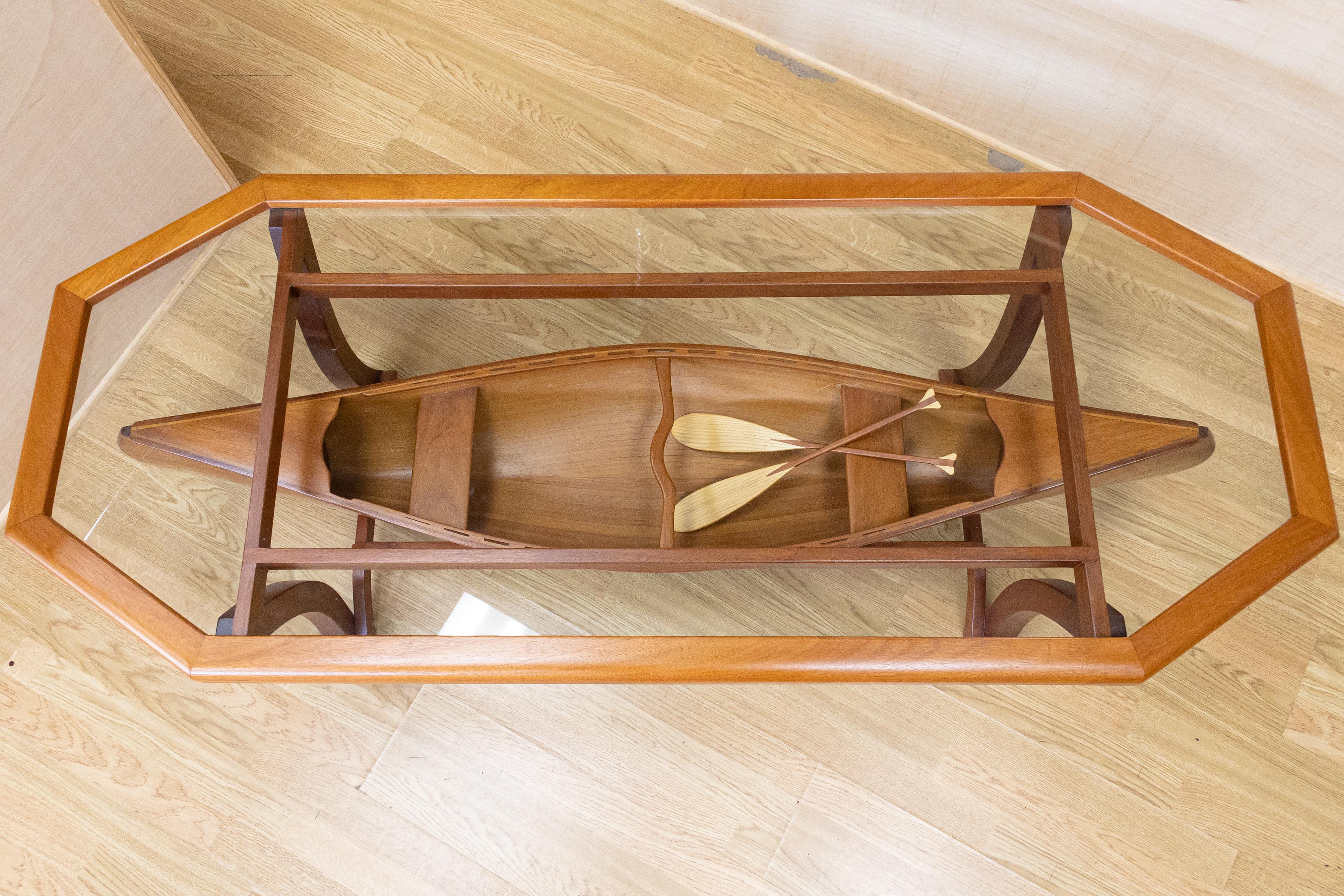 A very unique, custom made wood and glass boat table. This piece is made up of three pieces; the table top glass with wood frame, the canoe with paddles, and the base frame. Each of these items sit together without assembly. This item is in very