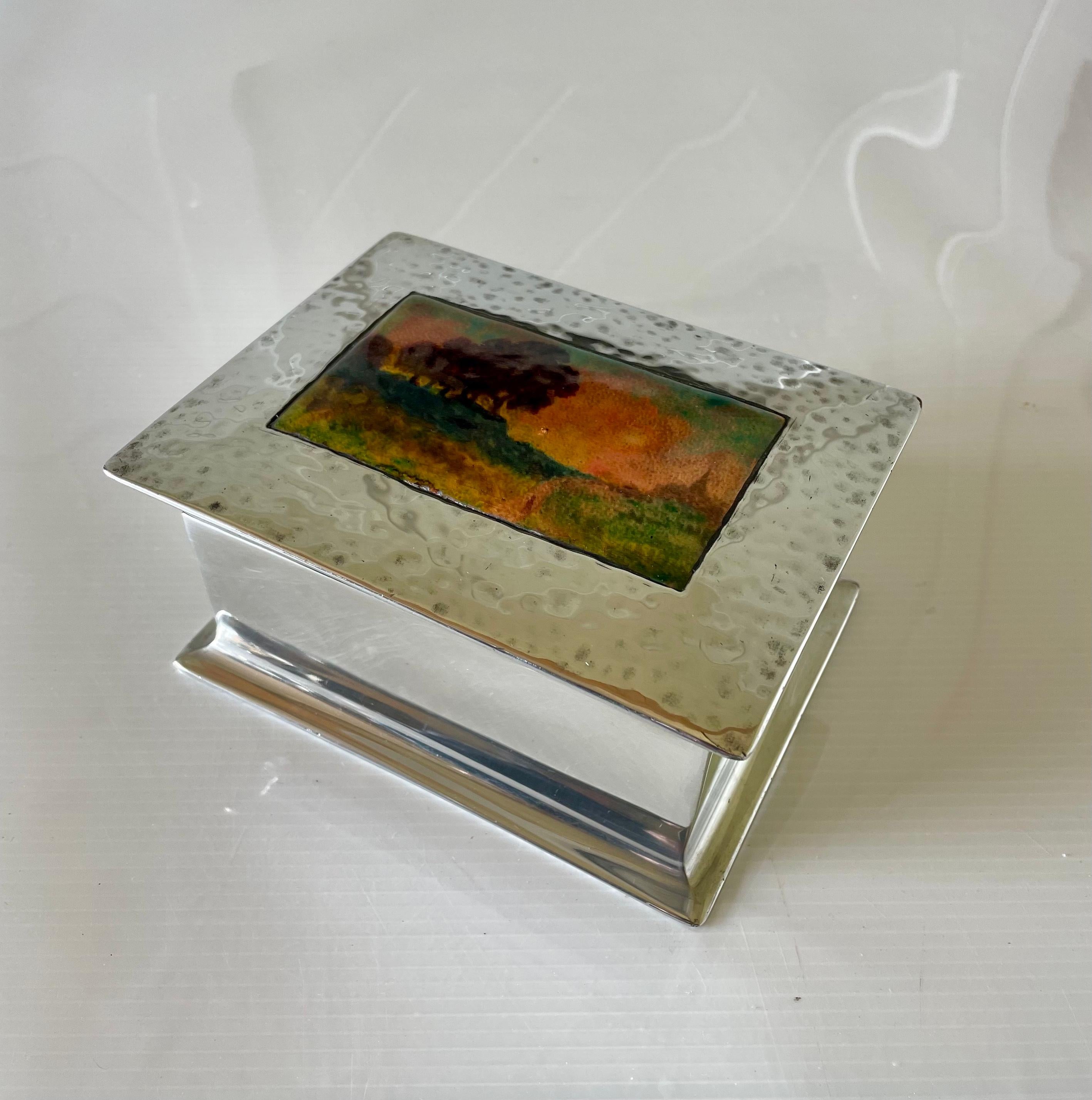 Arts & Crafts opening pewter box with enamel panel to lid

Wood lined

Panel depicting a country scene of trees and road leading to a country church

Panel design attributed to Fleetwood Varley

Liberty & Co ‘Tudric’ No 082

Circa 1900

Height 7cm.