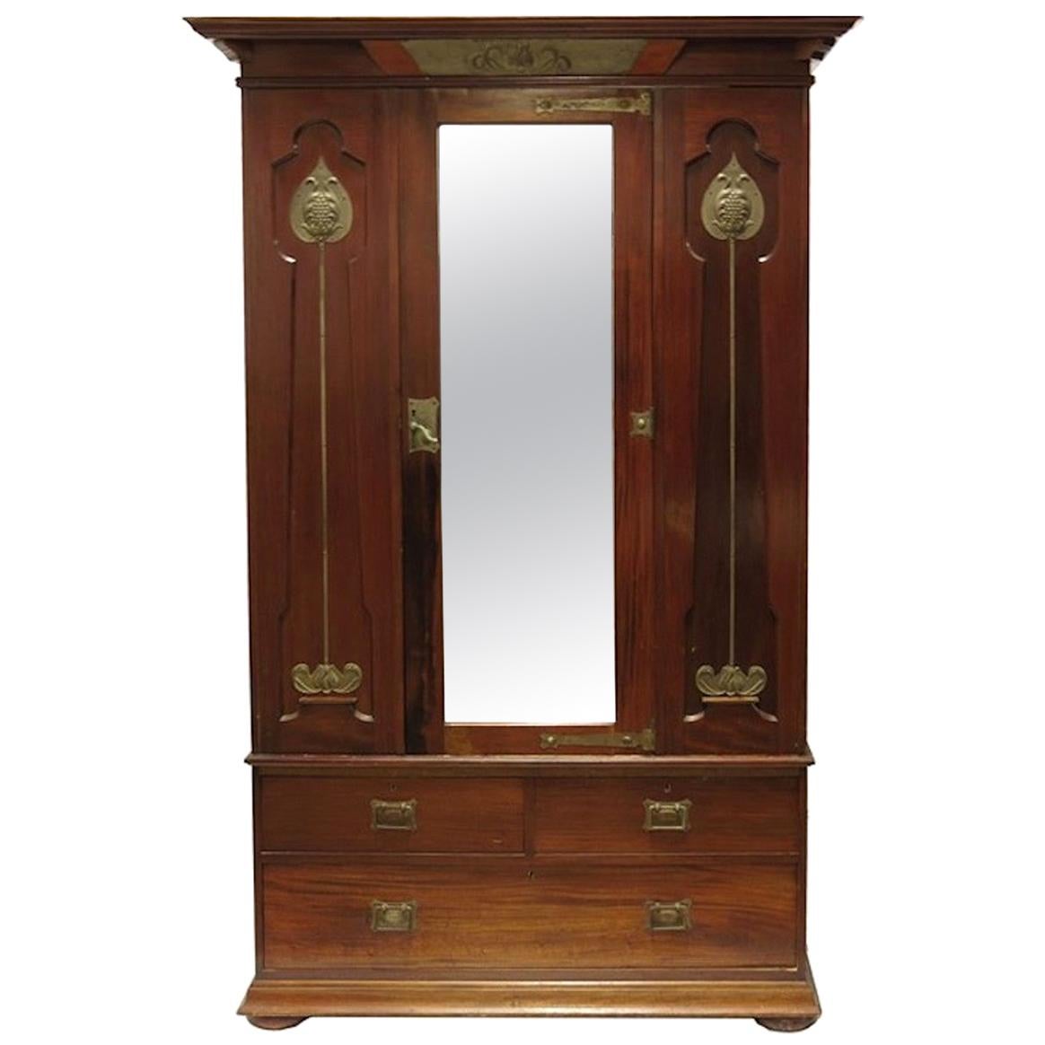 Arts & Crafts mahogany mirrored wardrobe by Shapland & Petter, circa 1920, the overhanging cornice with silvered panel to the centre over central mirrored door flanked by embossed silvered poppy panels, hanging rails and hooks enclosed in the Art
